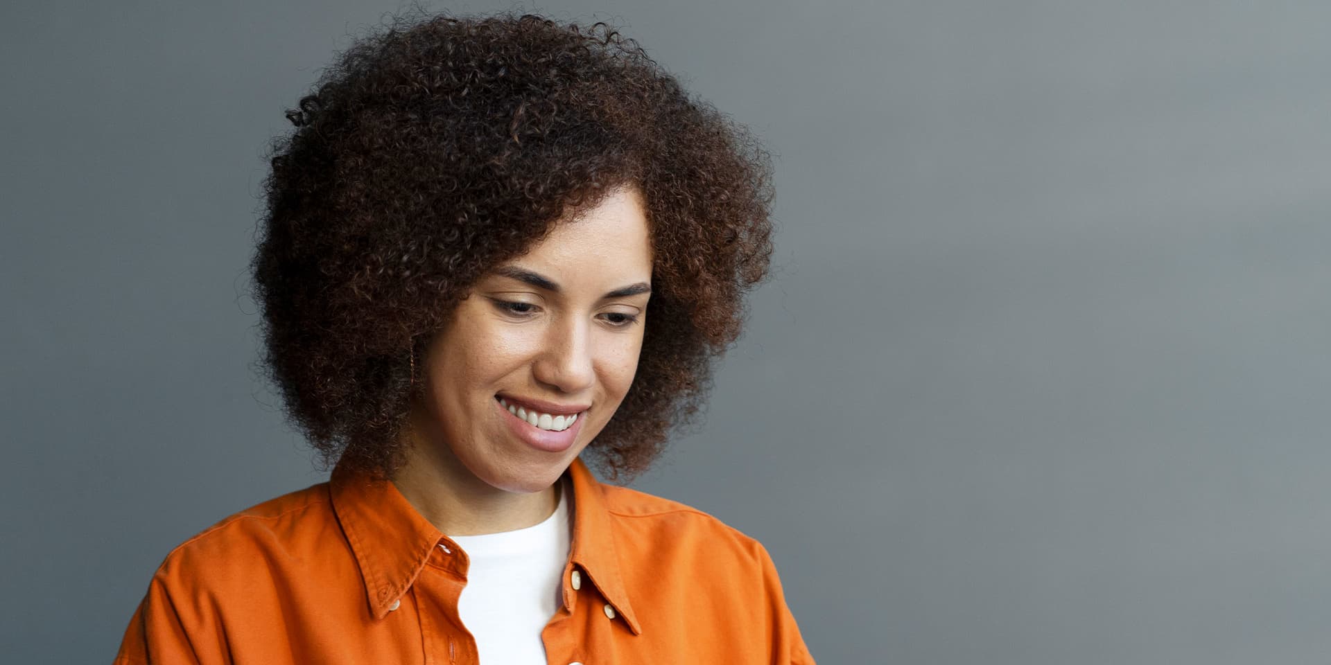 A woman sitting on the sofa, smiling and looking at her laptop.