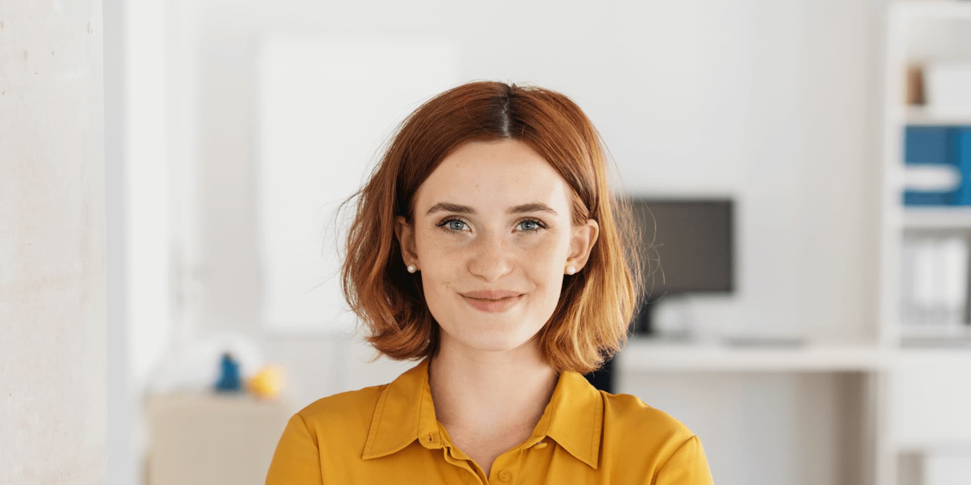 Smiling woman stands in office with arms crossed.