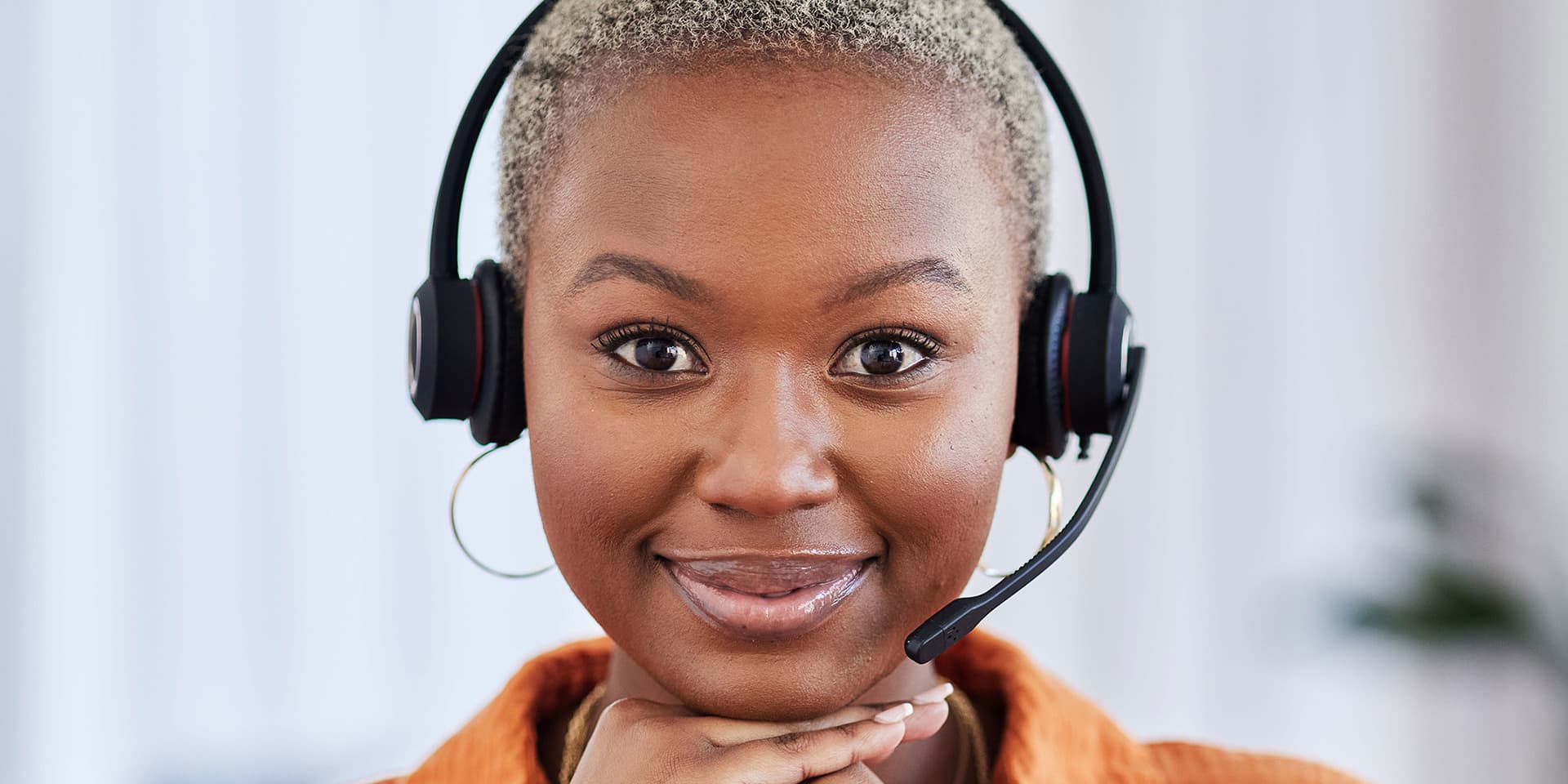 Young woman sitting wearing a headset and her hands on her chin, smiling.