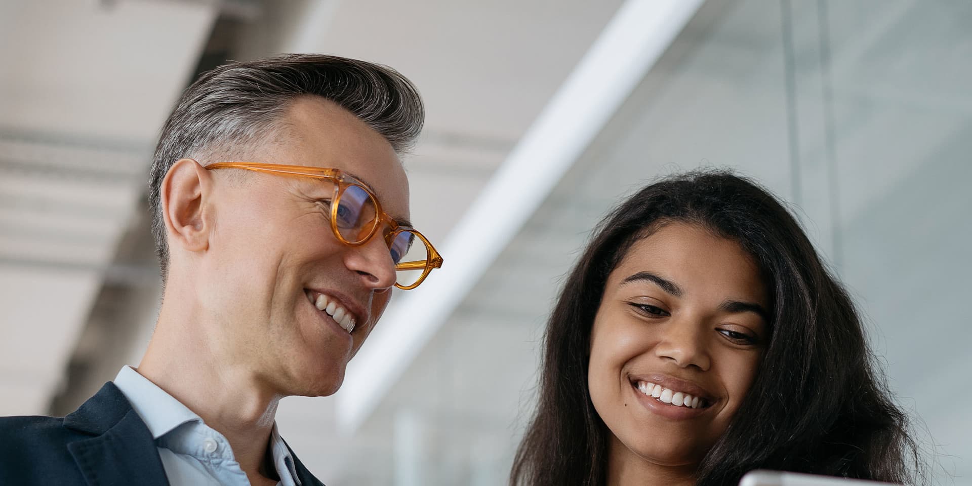 A man and a woman standing and smiling at an ipad.