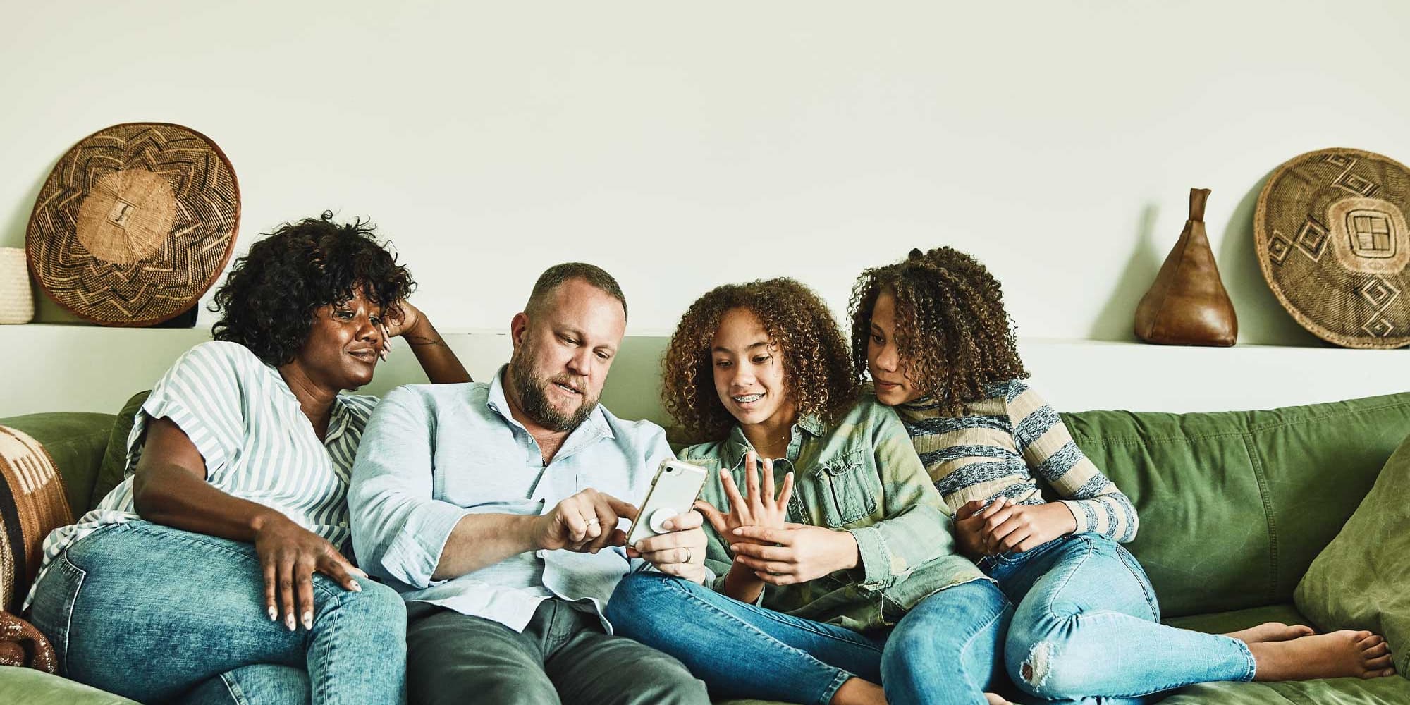 Titelbild Infoseite Infos für Eltern: Eltern mit Kindern sitzen auf dem Sofa und schauen gemeinsam auf Smartphone