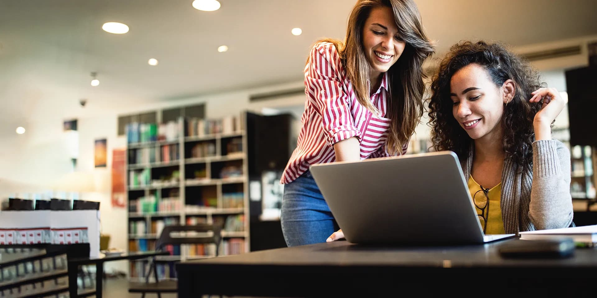 Titelbild zum Artikel "Künstliche Intelligenz in Schulen und Unis": Zwei Studentinnen sitzen in Bibliothek