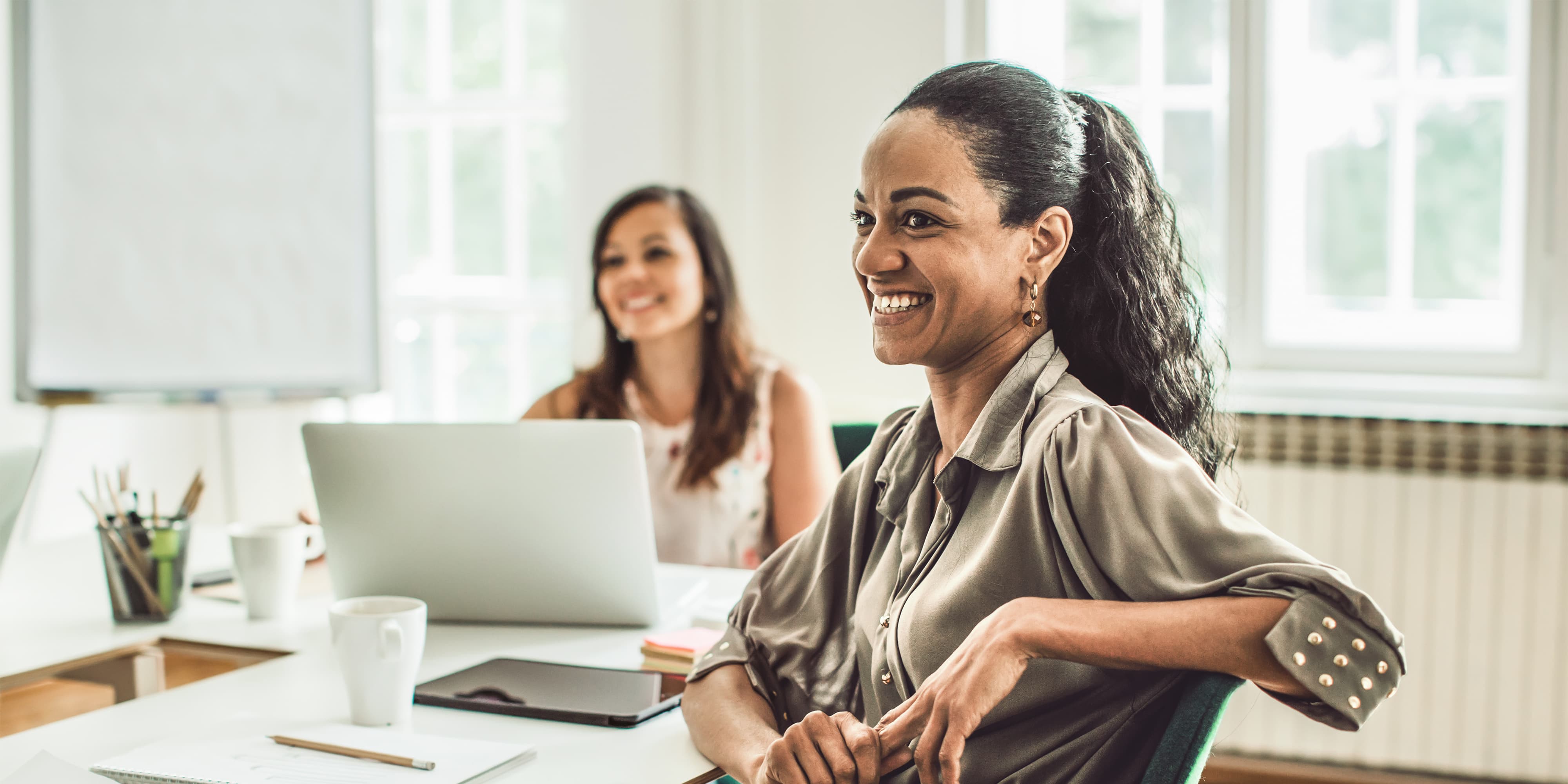 Two individuals are seated in a bright office with laptops and notebooks, engaged in a discussion, illustrating a collaborative study environment for an MBA in finance in Germany.