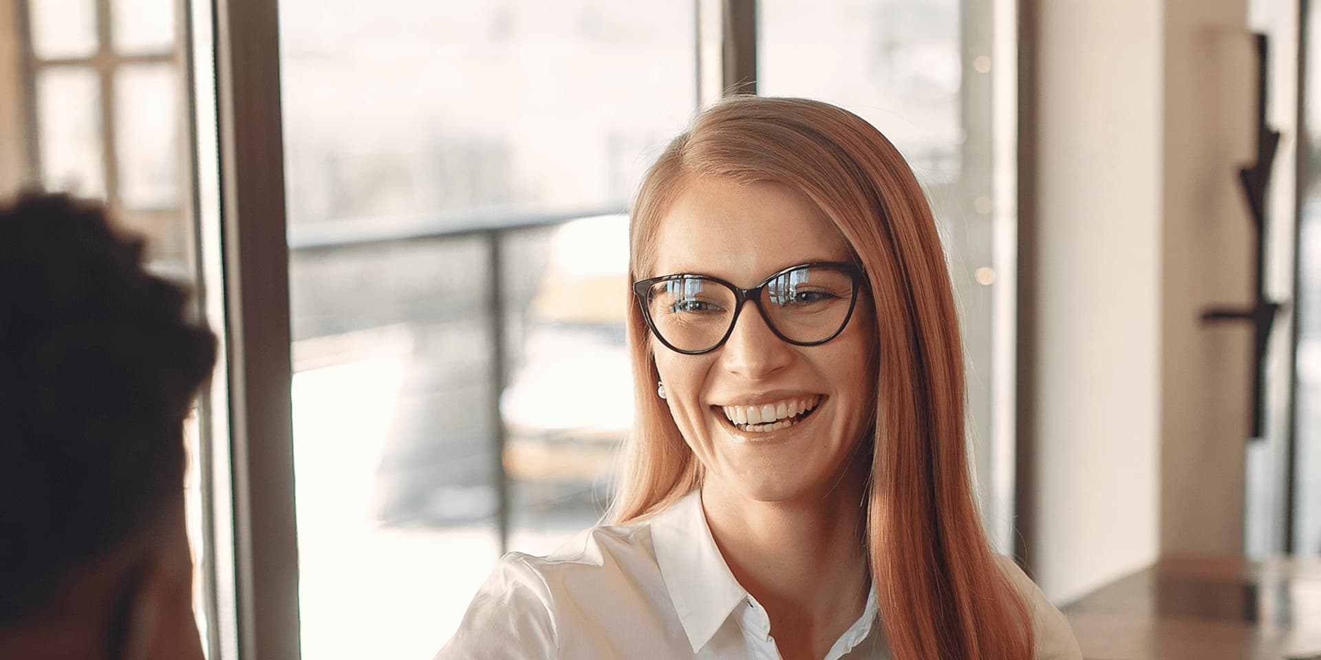 A smiling woman wearing glasses is sat down facing a man, engaging in a conversation about trade finance.