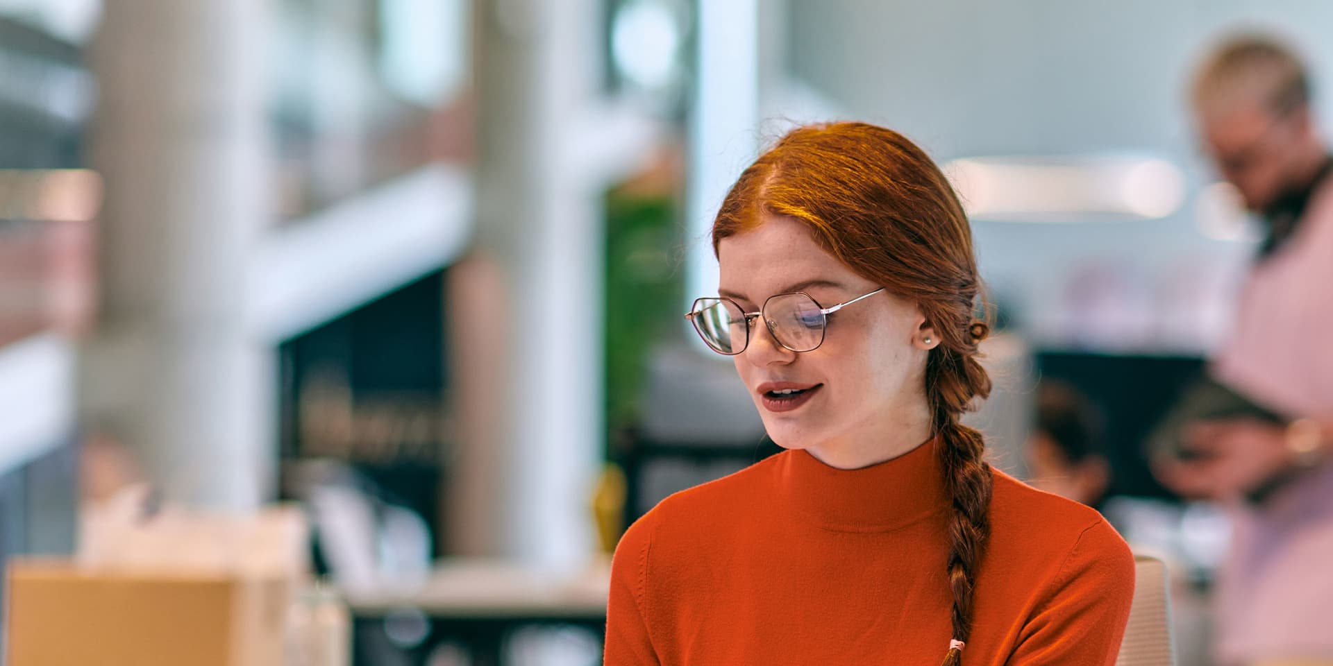 A young woman wearing glasses is sitting at a desk and typing on her laptop.