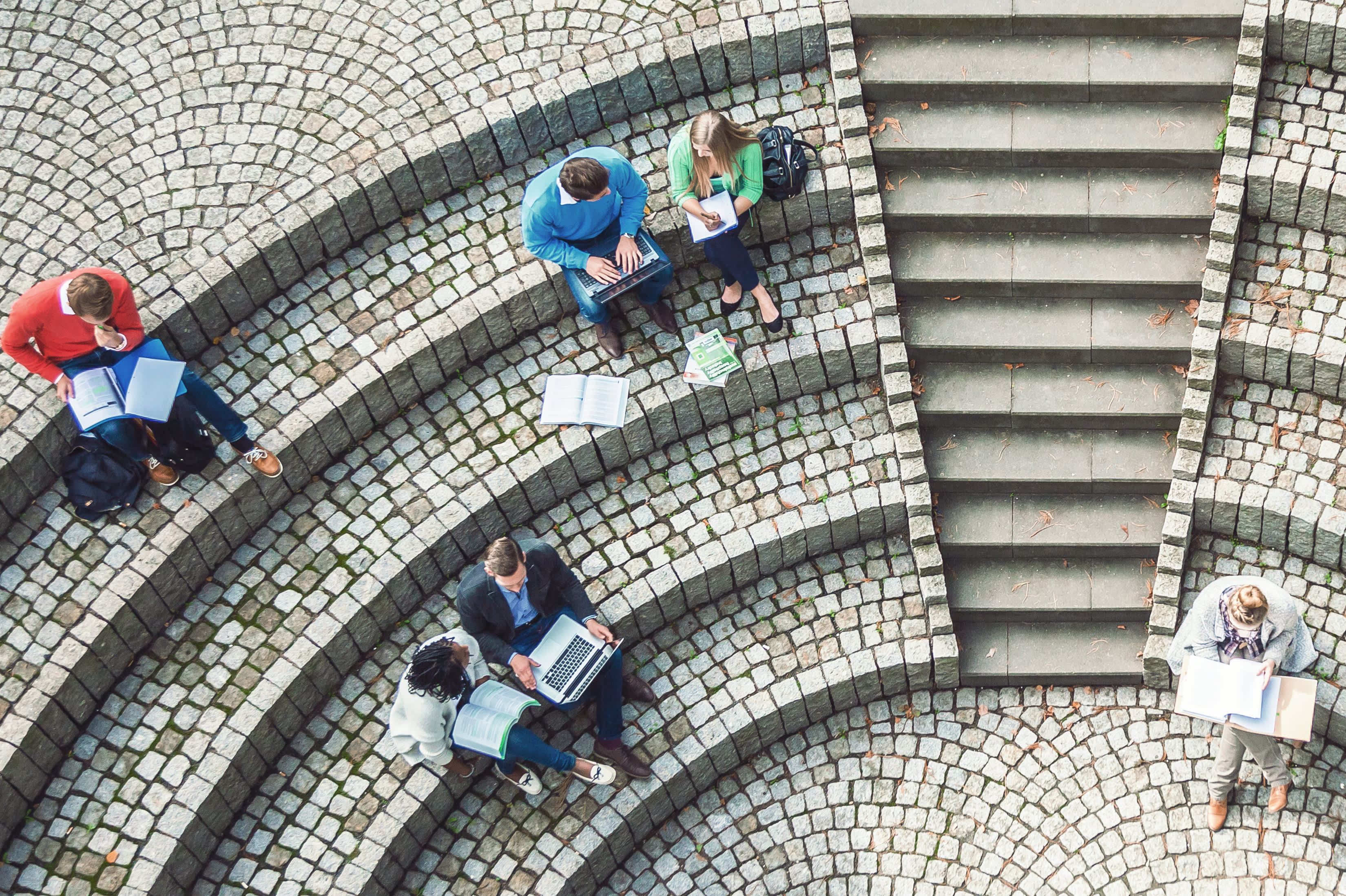Titelbild für Infoseite "Duales Studium Die Hochschule": Studenten auf Treppen schauen auf einen Laptop