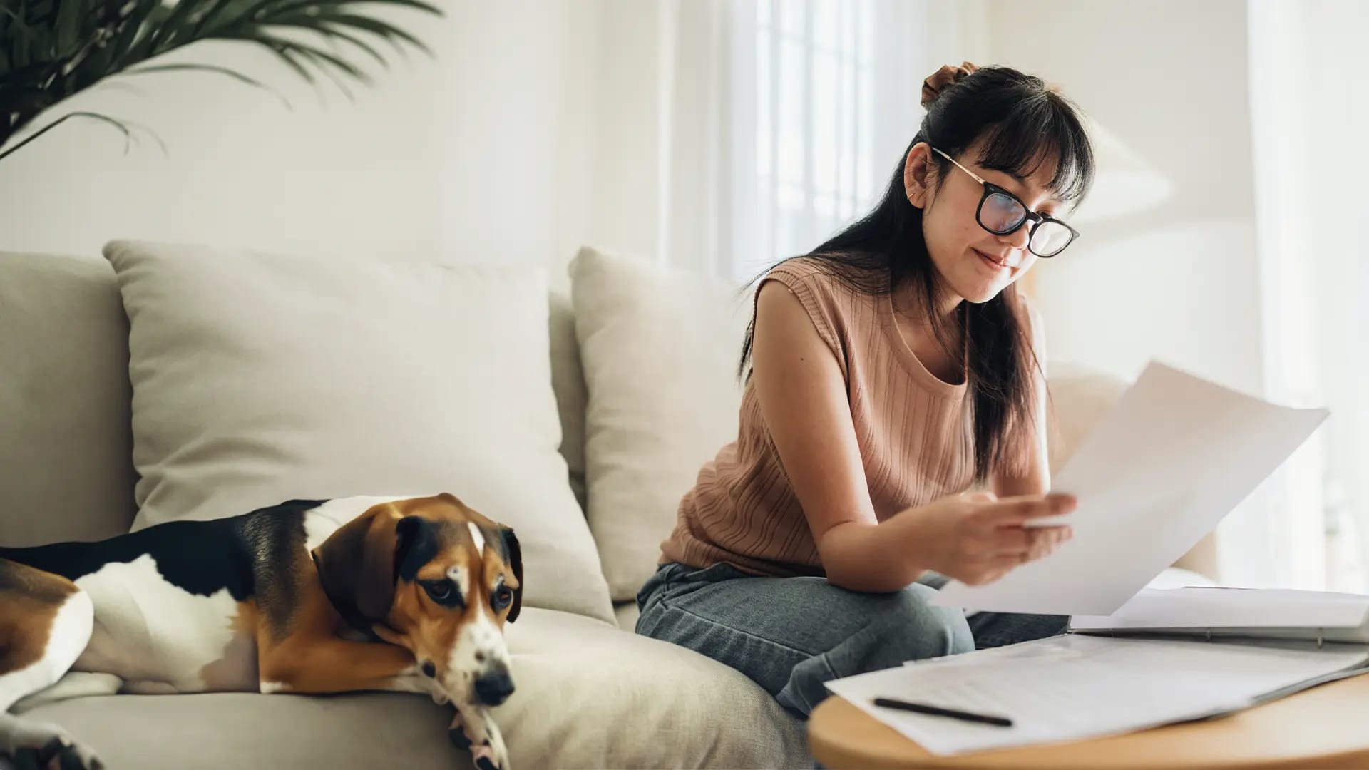 Titelbild zum Artikel "Geld anlegen für Anfänger": Frau sitz auf dem Sofa und schaut sich Dokumente an