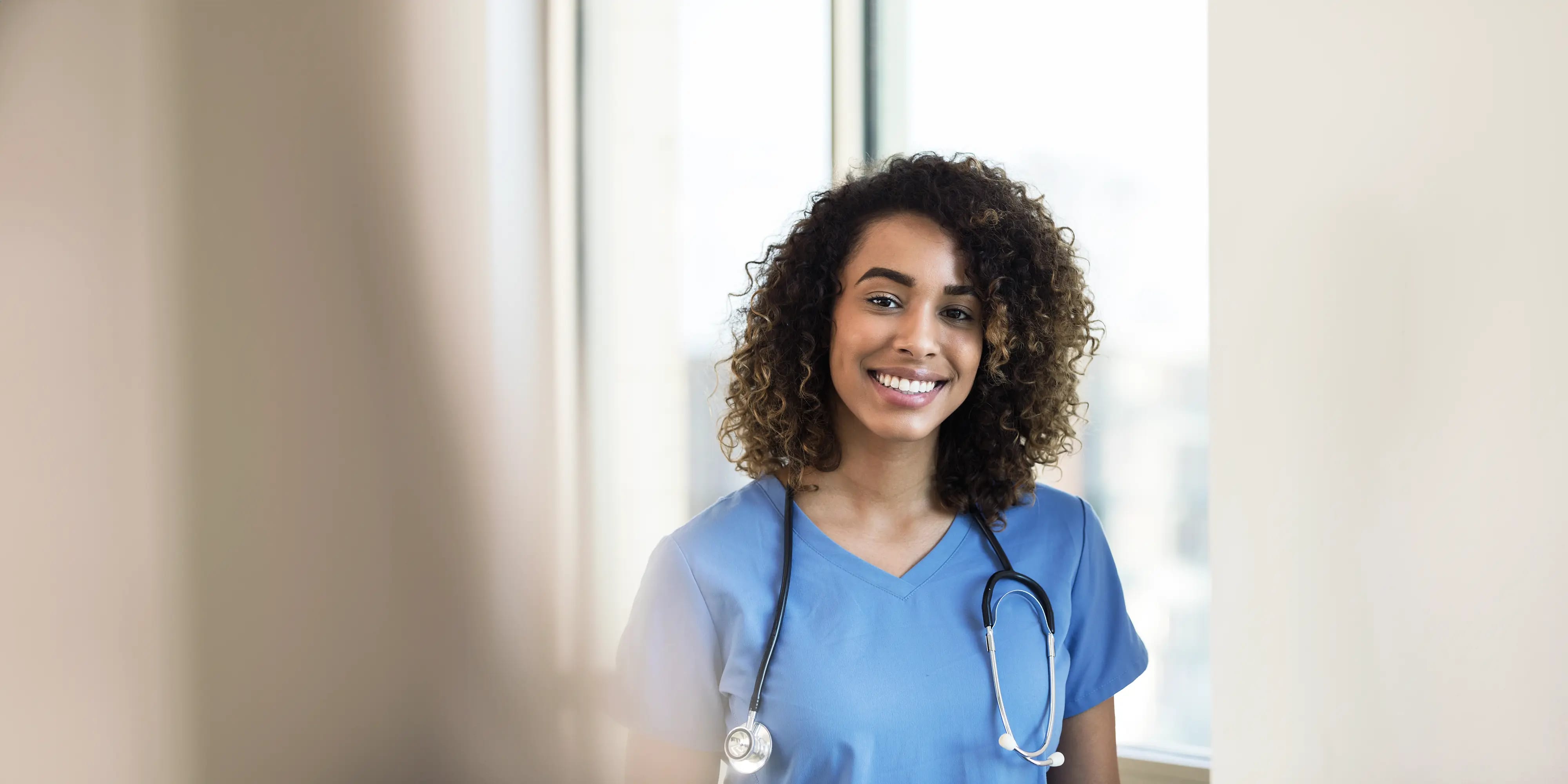 Titelbild der Infoseite "Fernsudium Pflegefachkraft": Studentin lacht und hat ein Stethoskop um den Hals