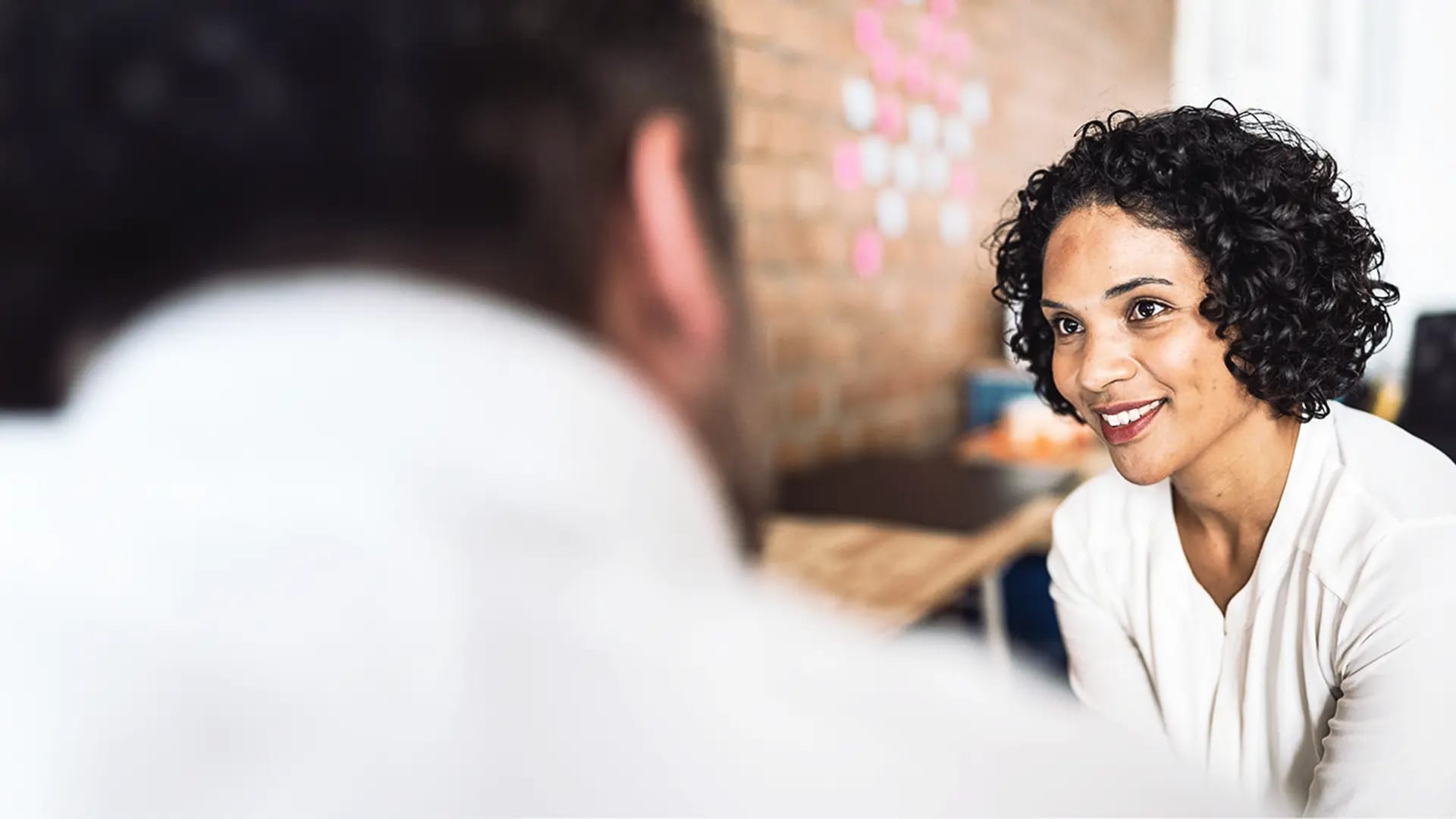 Titelbild zum Artikel "6 Fragen zum IU Psychologie-Studium": Studentin im IU Psychologie-Studium im Gespräch mit Professor in Vorlesungssaal, lächelt freundlich.