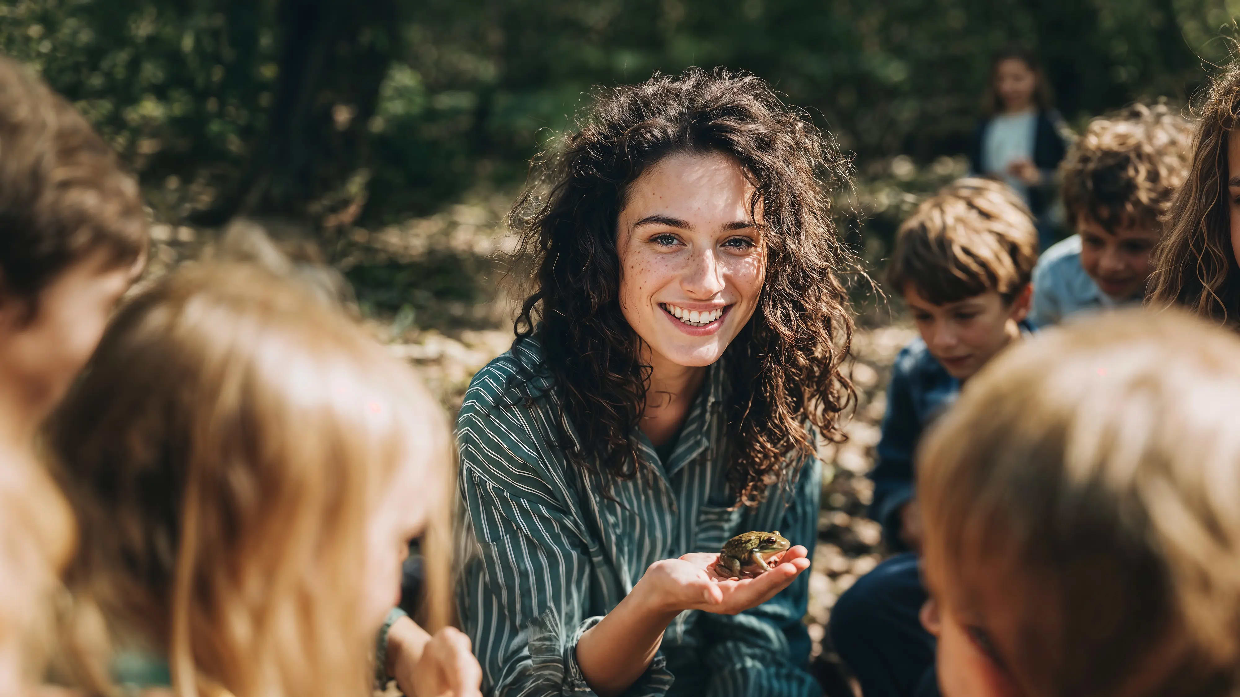 Bachelor Kindheitspädagogik: Frau mit Gruppe von Kindern im Garten mit kleinem Frosch in der Hand