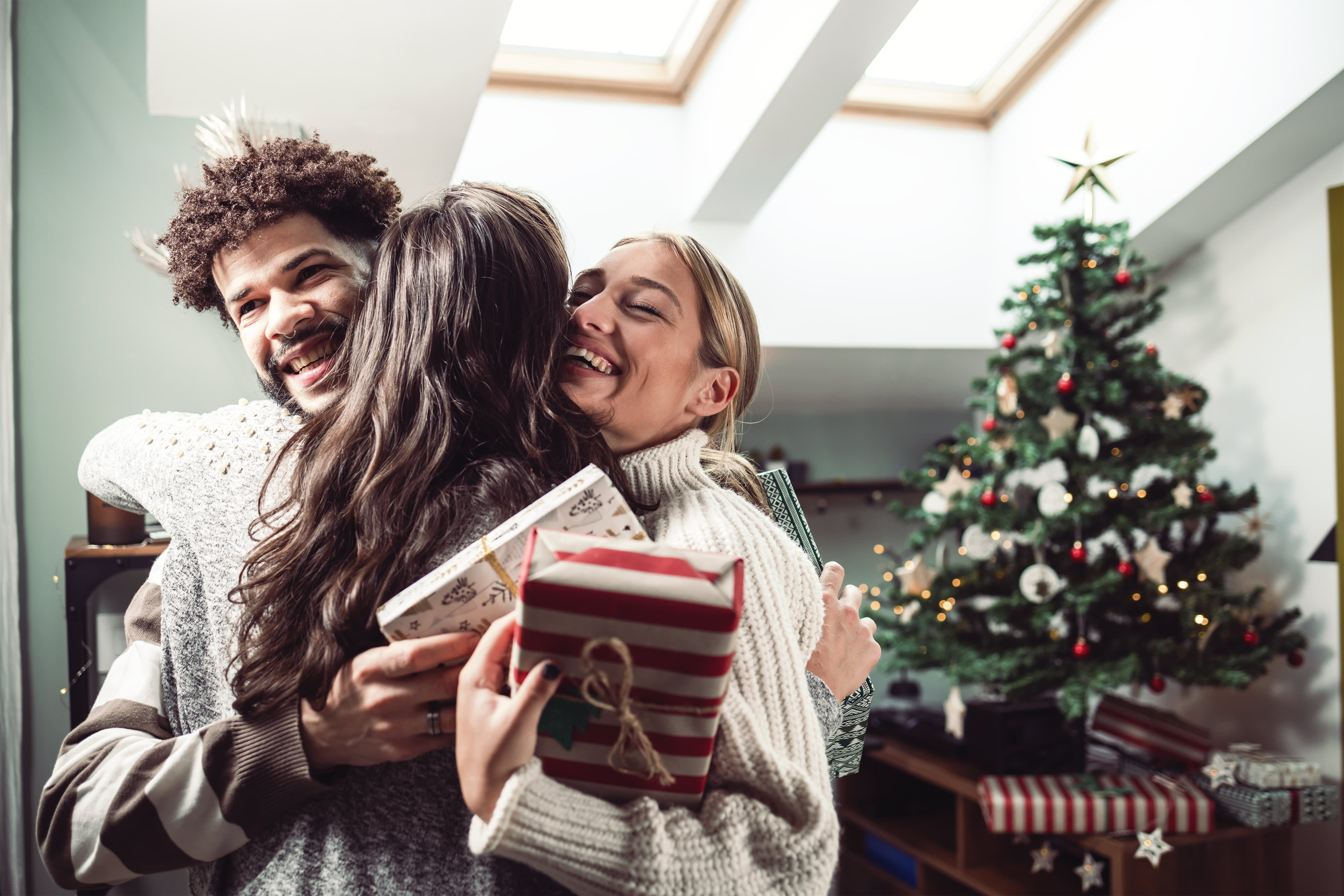 Titelbild für Infoseite zur Kampagne "Gemeinsame Zeit": Freunde umarmen sich mit Geschenken in der Hand, im Hintergrund steht ein Weihnachtsbaum.