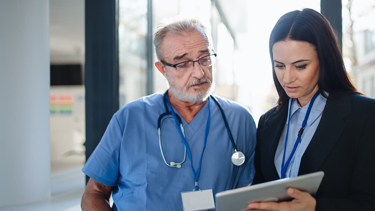 A healthcare professional in a blue uniform and stethoscope collaborates with a businessperson holding a tablet, illustrating teamwork in mba in healthcare management in Germany.
