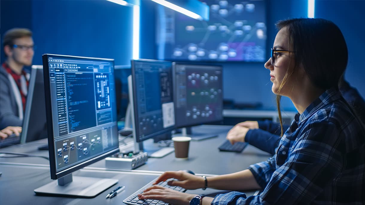 A person focuses on multiple computer screens displaying code and network visuals in a cybersecurity lab, highlighting studies related to a masters in cyber security in Germany.
