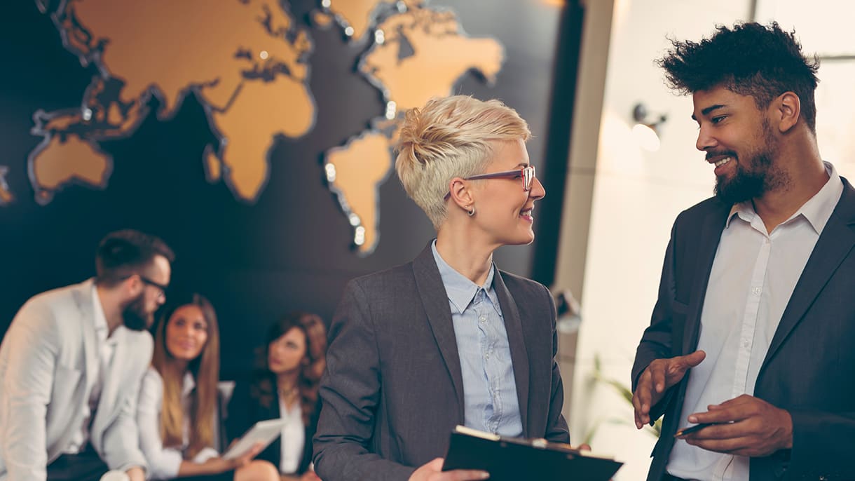 Two business professionals engage in a discussion with a world map in the background, representing the concept of international management in Germany.