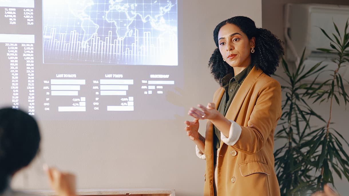 A person in a tan blazer gives a presentation on international market data in a classroom setting, highlighting aspects of an international management bachelor online program.