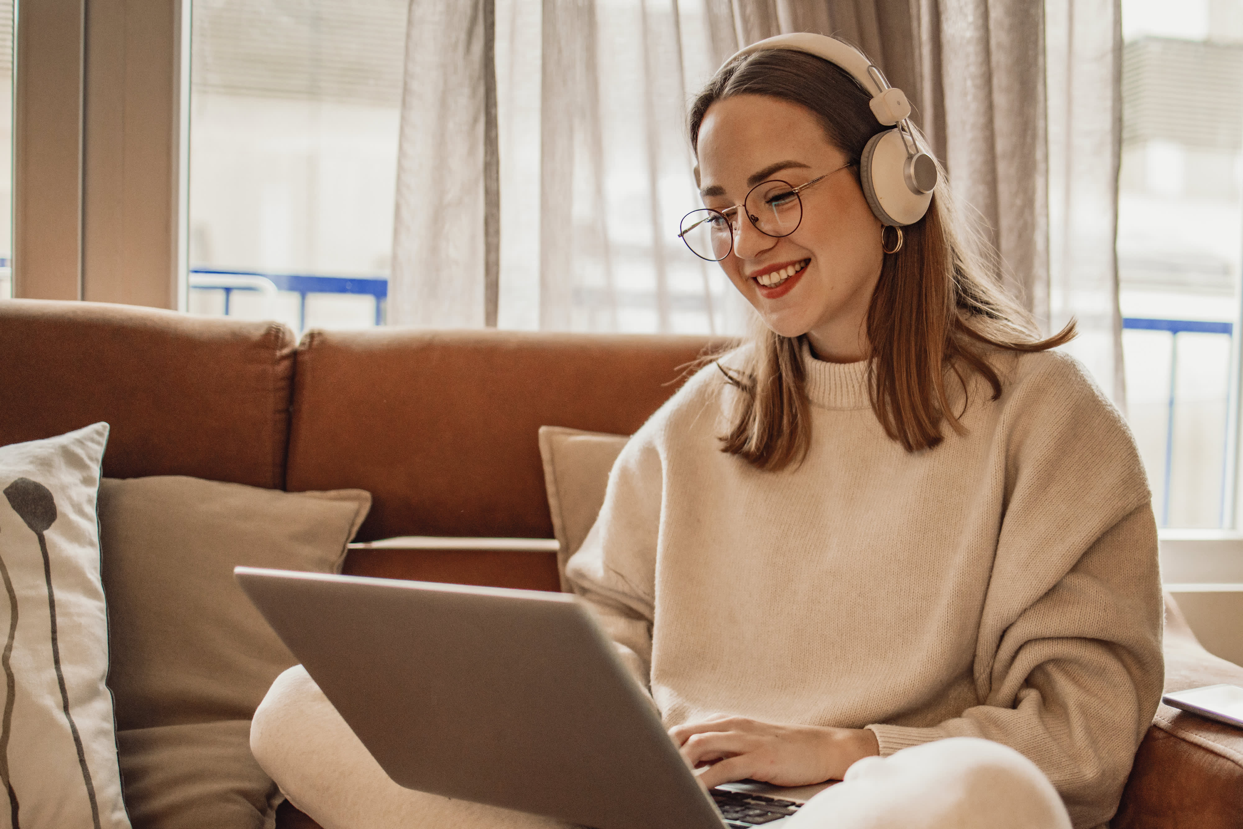 Titelbild der Infoseite "Duales Studium Lebenslauf": Studentin sitzt mit glücklich mit Kopfhörern vor ihrem Laptop
