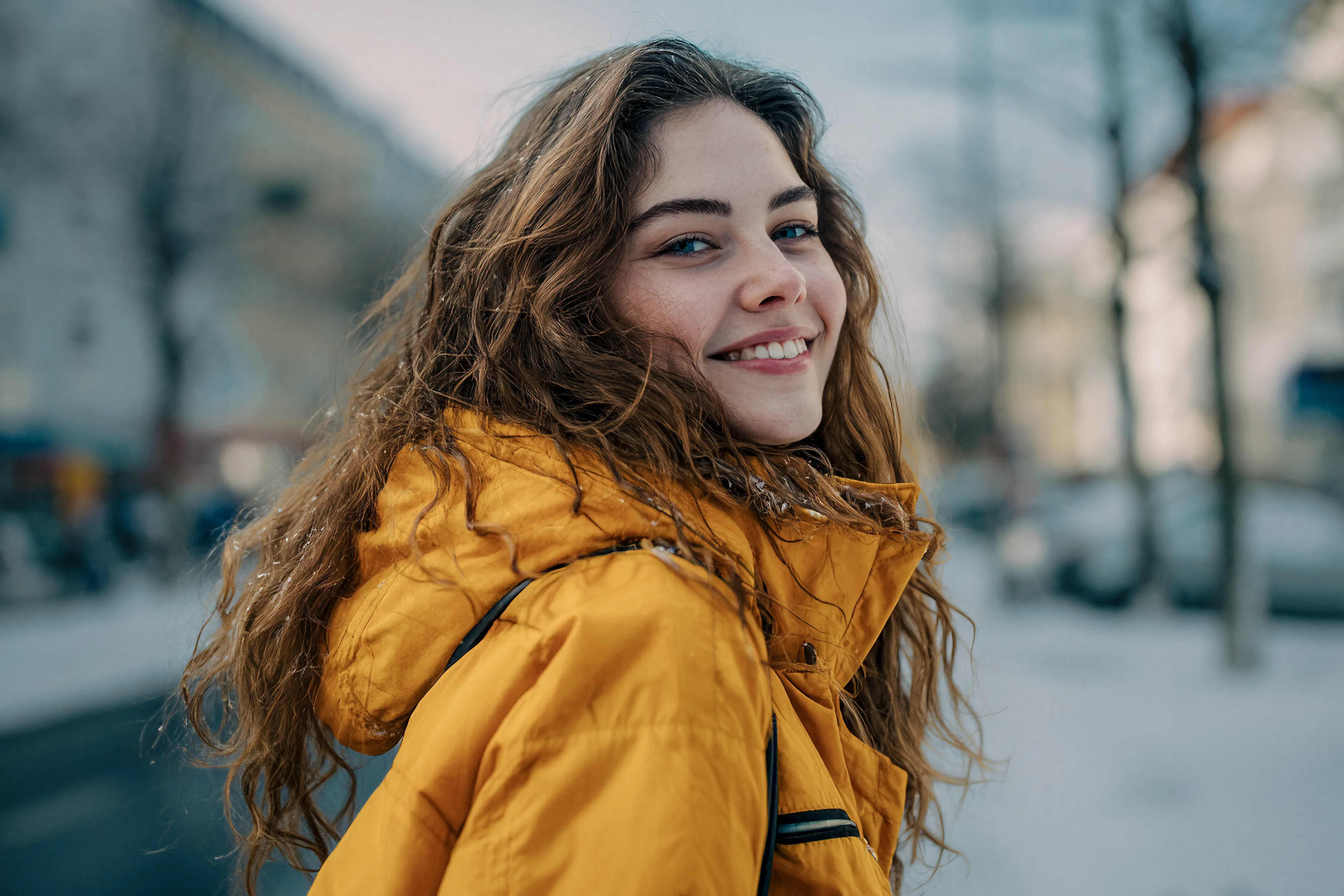 Junge Frau mit gelbem Mantel lächelt in urbaner Umgebung