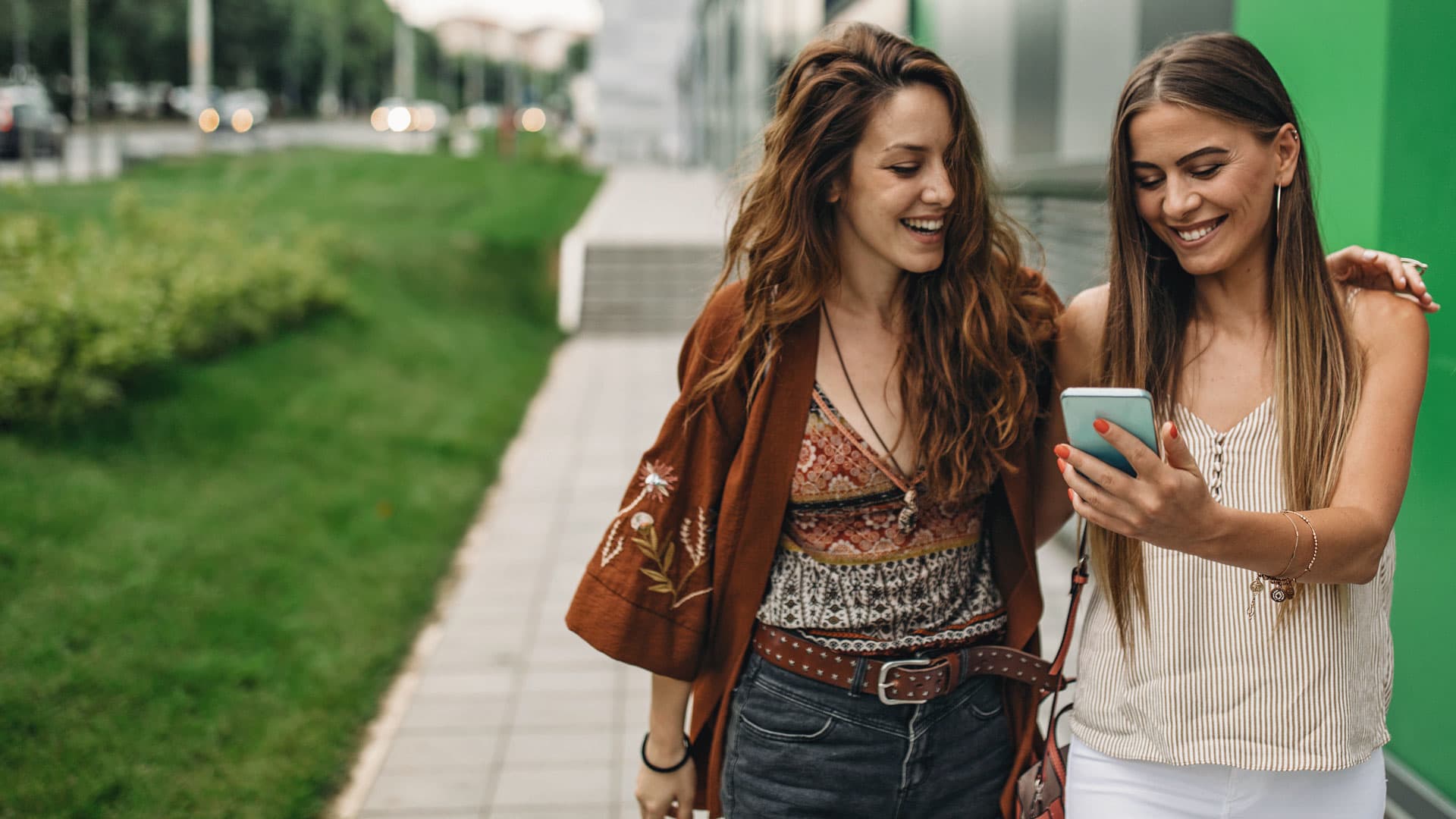 Zweit sich umarmende Studentinnen schauen auf ihr Smartphone