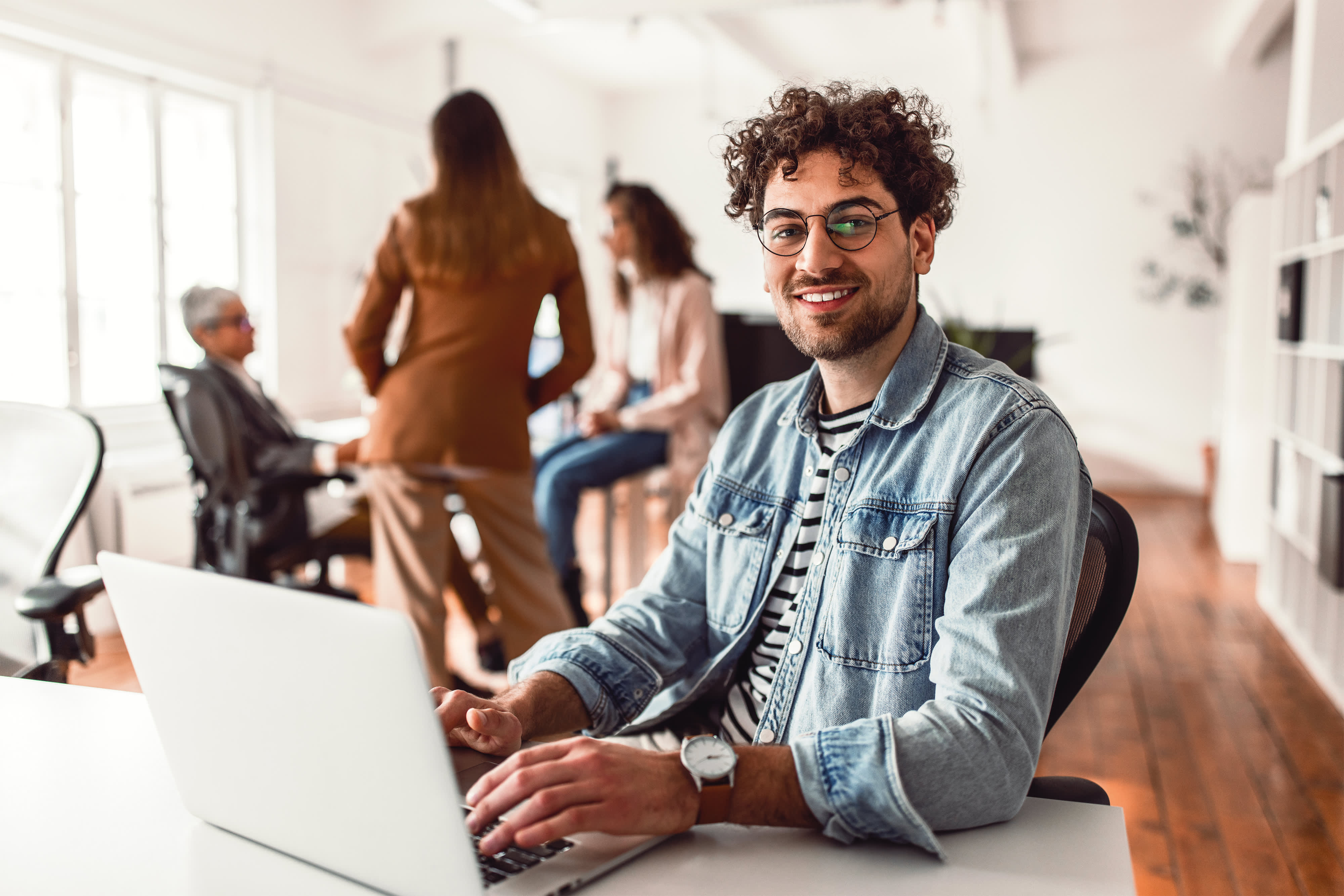 Titelbild für Infoseite "Bewerbung duales Studium Soziale Arbeit": Studieninteressierter sitzt in einem Büro am Schreibtisch und schaut sich am Laptop den Bewerbungsprozess für ein duales Studium im Bereich Soziale Arbeit an