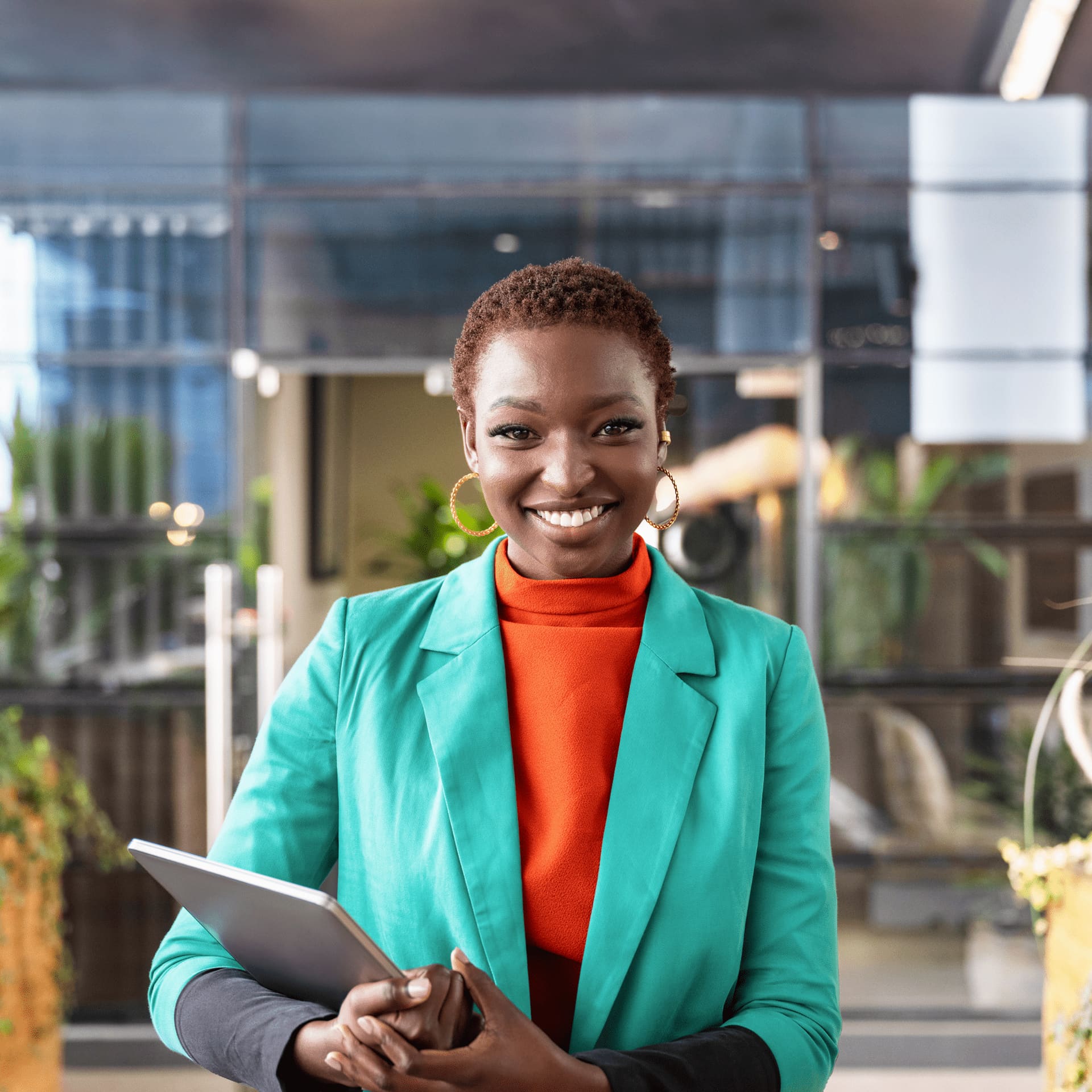 Smiling woman standing outside in formal blazer holding tablet.