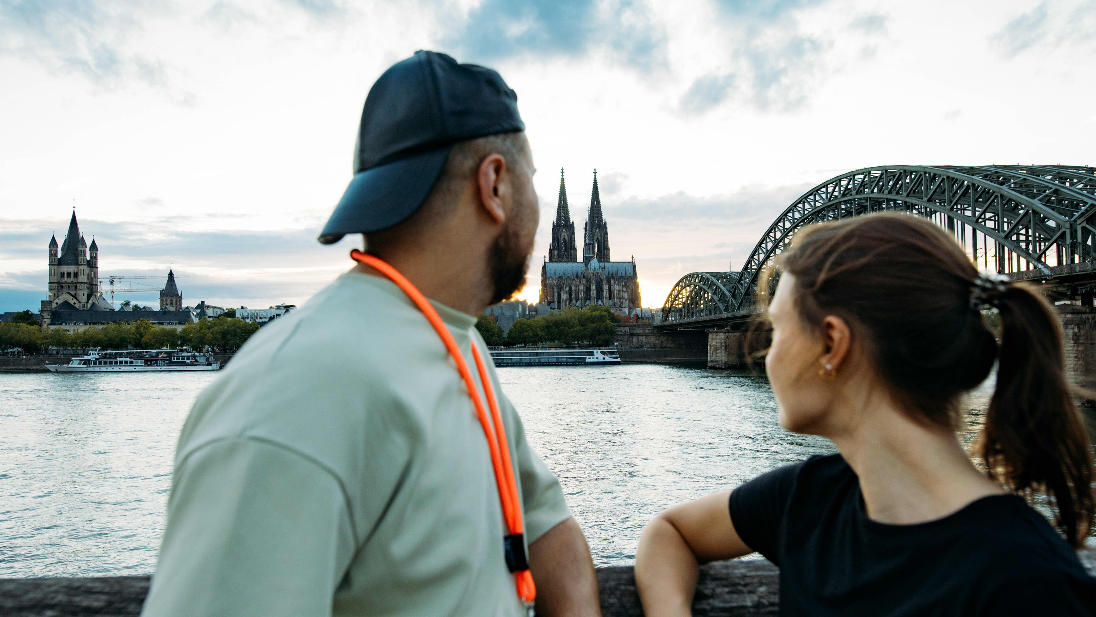 Two IU students looking at the Cologne skyline with Cologne Cathedral and the Hohenzollern Bridge across the Rhine River.
