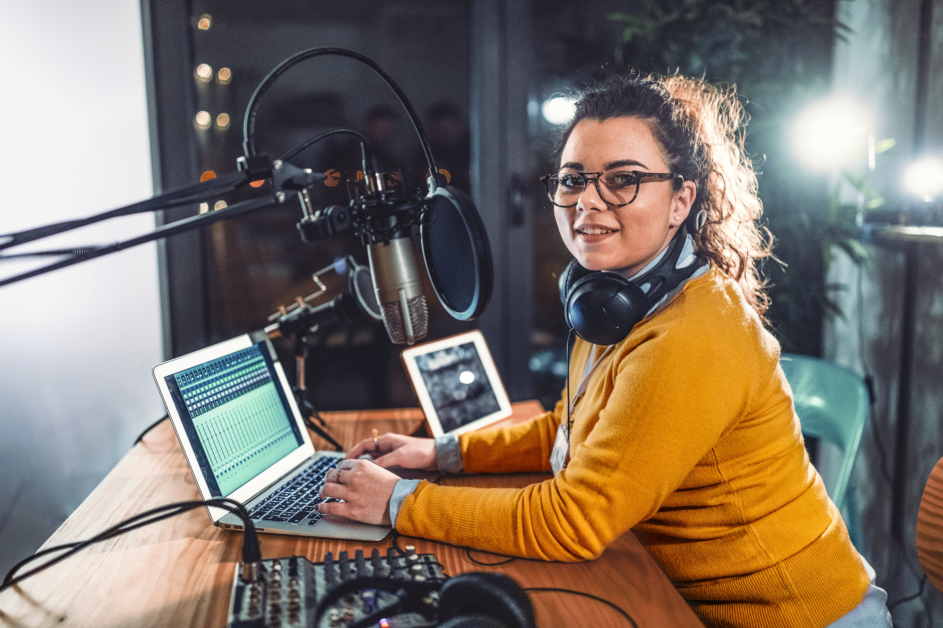 Titelbild für Infoseite “duales Studium Kommunikation und PR": Duale Studentin mit Brille trägt Kopfhörer, hat ein Mikrofon vor sich und sitzt im Aufnahme-Studio