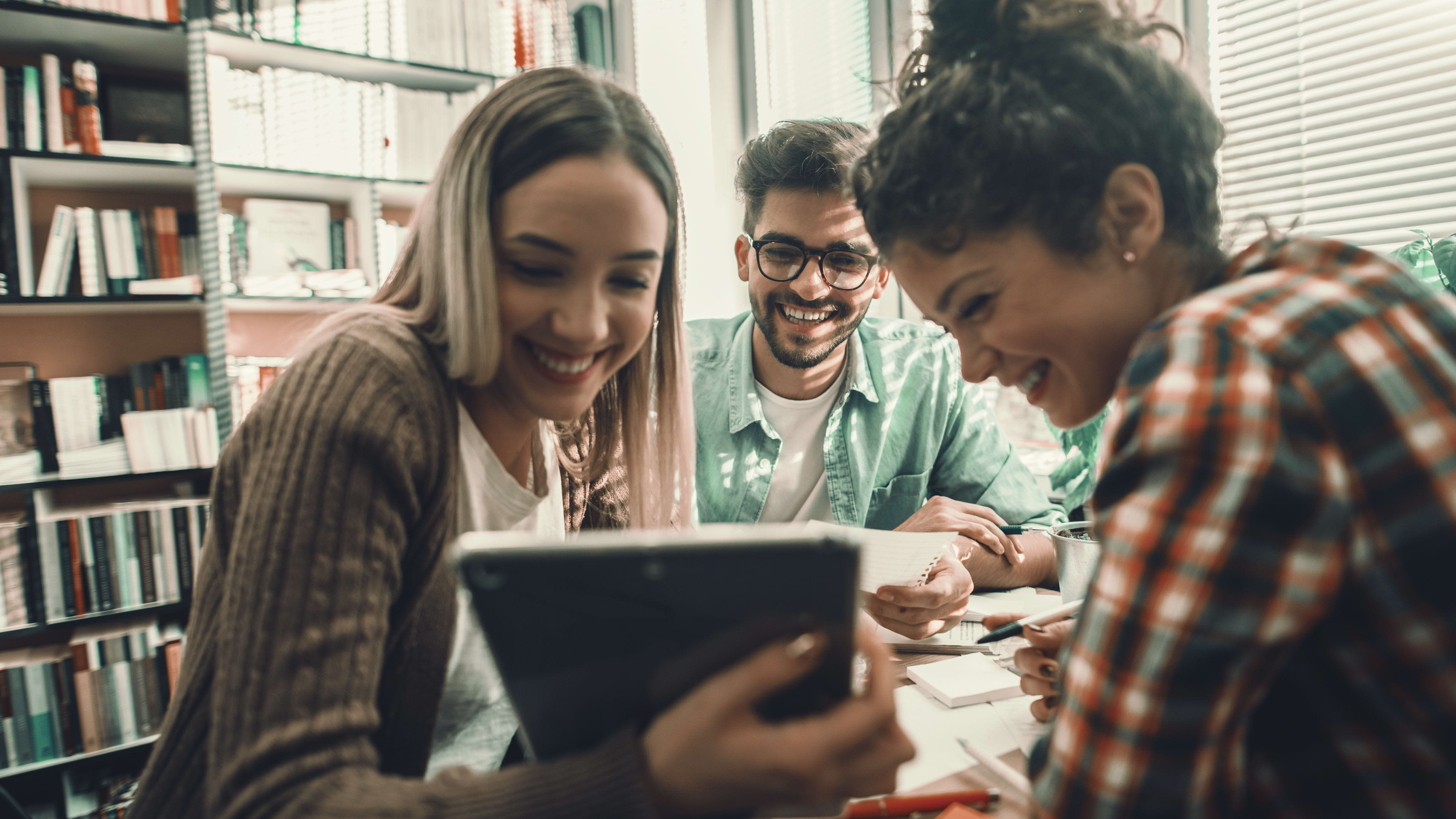 Titelbild der Infoseite "Duales Studium Sales Management": Drei Studierende aus dem Bereich Sales Management sitzen in der Bibliothek und lernen
