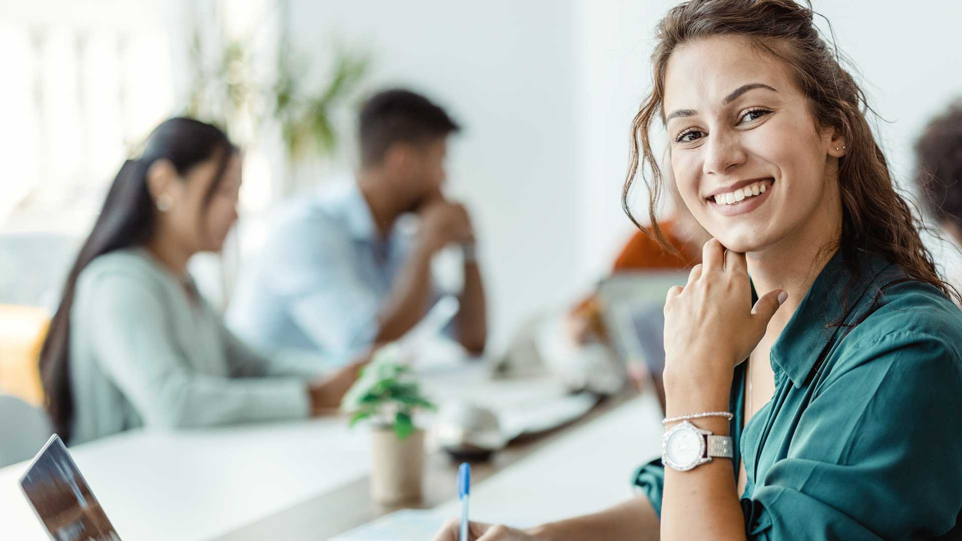 Titelbild zum Artikel "Erster Arbeitstag": Lächelnde Frau mit Laptop im Büro mit Kollegen