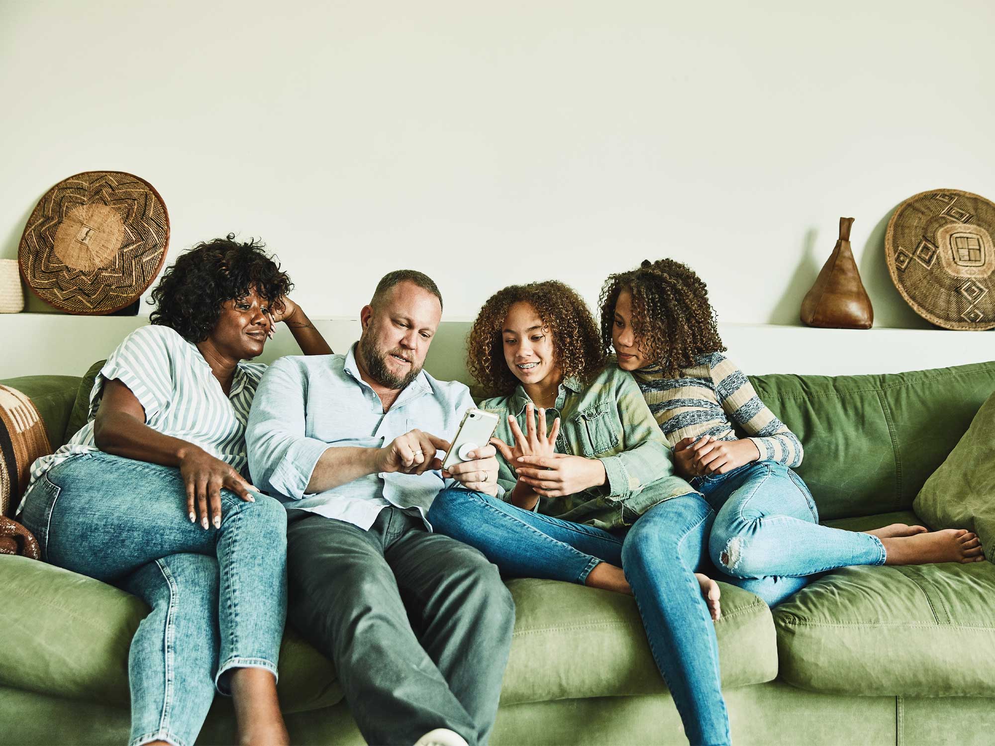 Titelbild Infoseite Infos für Eltern: Eltern mit Kindern sitzen auf dem Sofa und schauen gemeinsam auf Smartphone