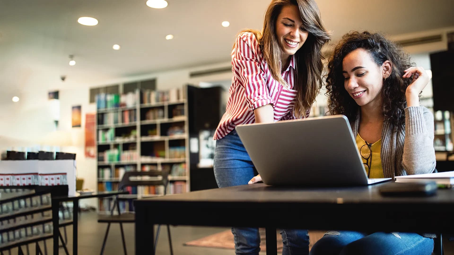 Titelbild zum Artikel "Künstliche Intelligenz in Schulen und Unis": Zwei Studentinnen sitzen in Bibliothek
