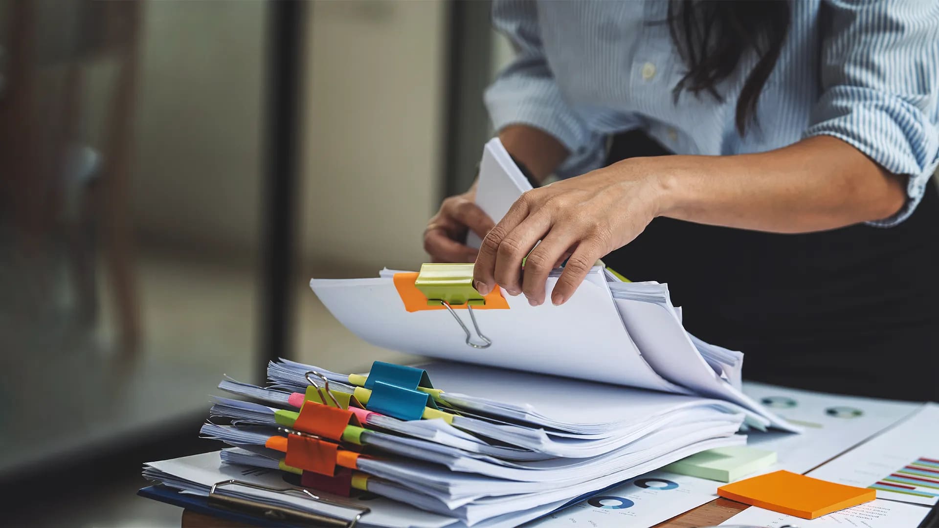 Titelbild zum Artikel "Nachhaltigkeit im Büro": Frau sortiert einen Stapel Unterlagen am Schreibtisch