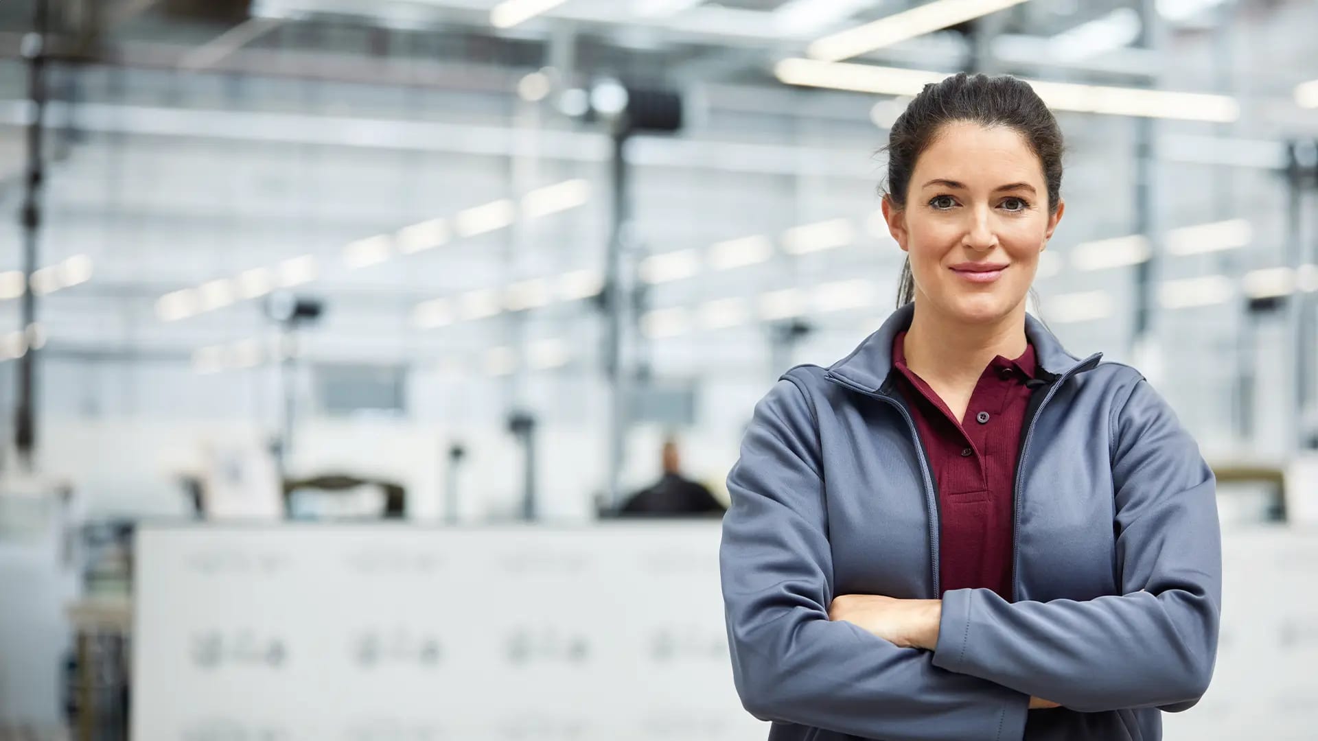Titelbild für Artikel zum Techniker Studium: Selbstbewusste junge Frau steht in einer Produktionshalle