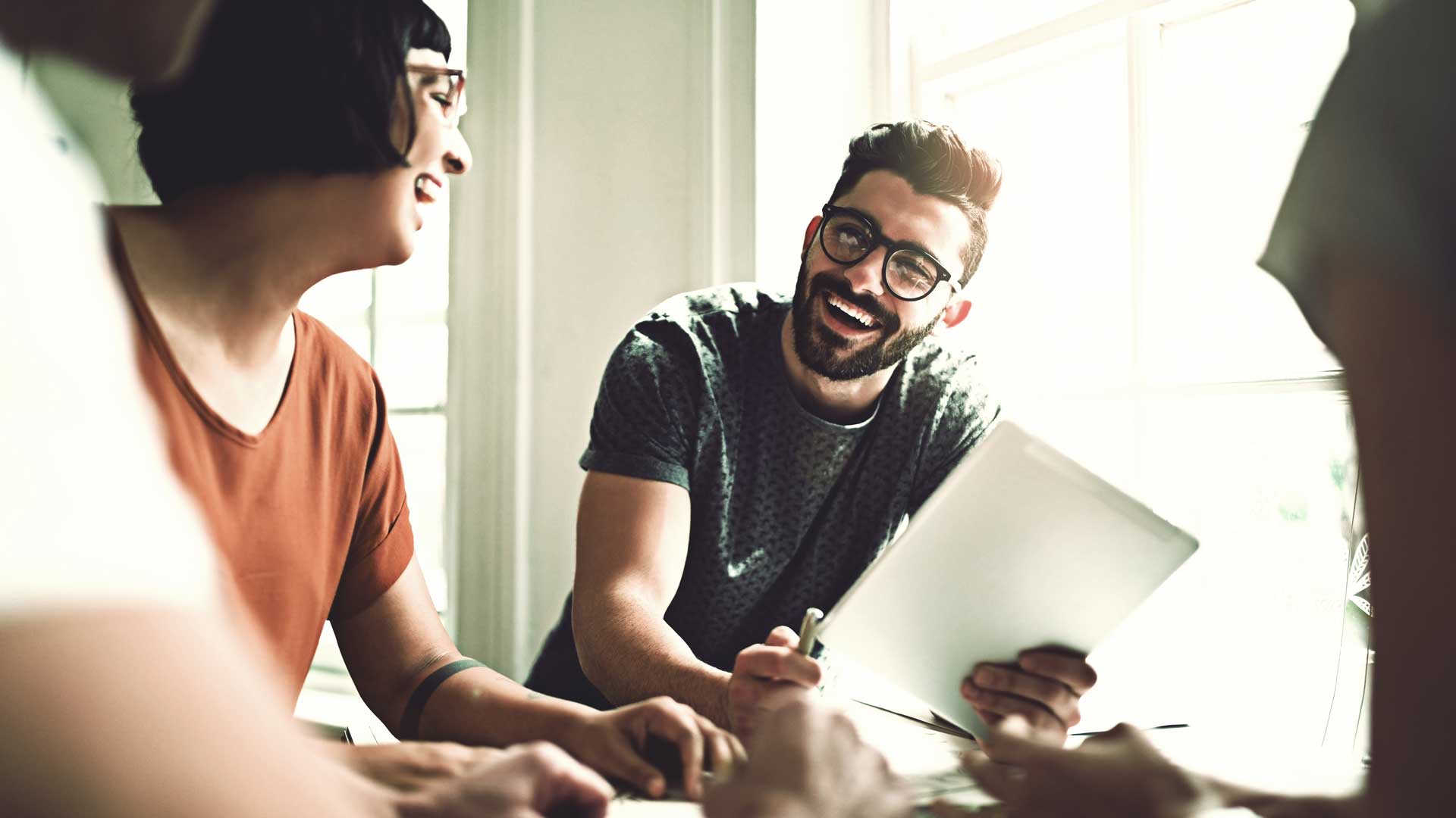 Titelbild zum Artikel "Unterschied Hochschule vs. Universität": 2 lächelnde Studenten am Schreibtisch