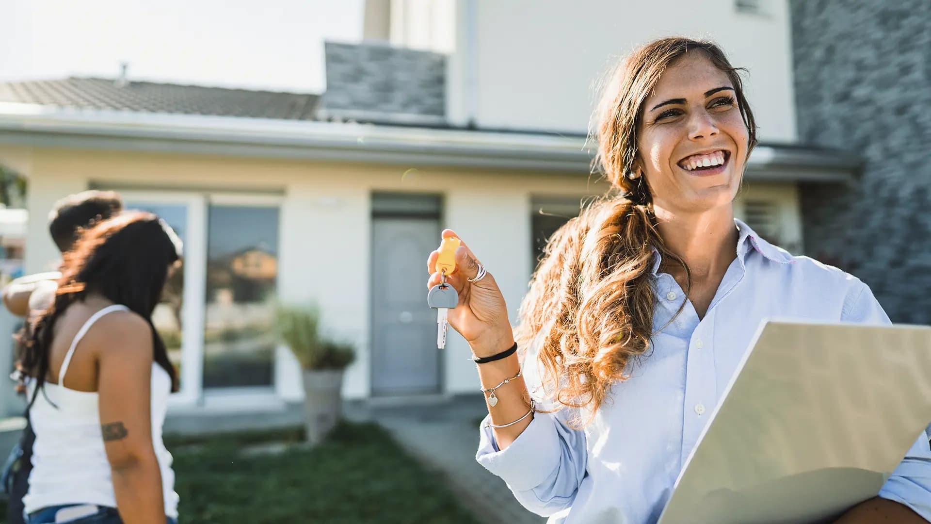 Titelbild zum Artikel "Wie wird man Immobilienmakler": Immobilienmaklerin mit Schlüssel in der Hand steht vor Haus
