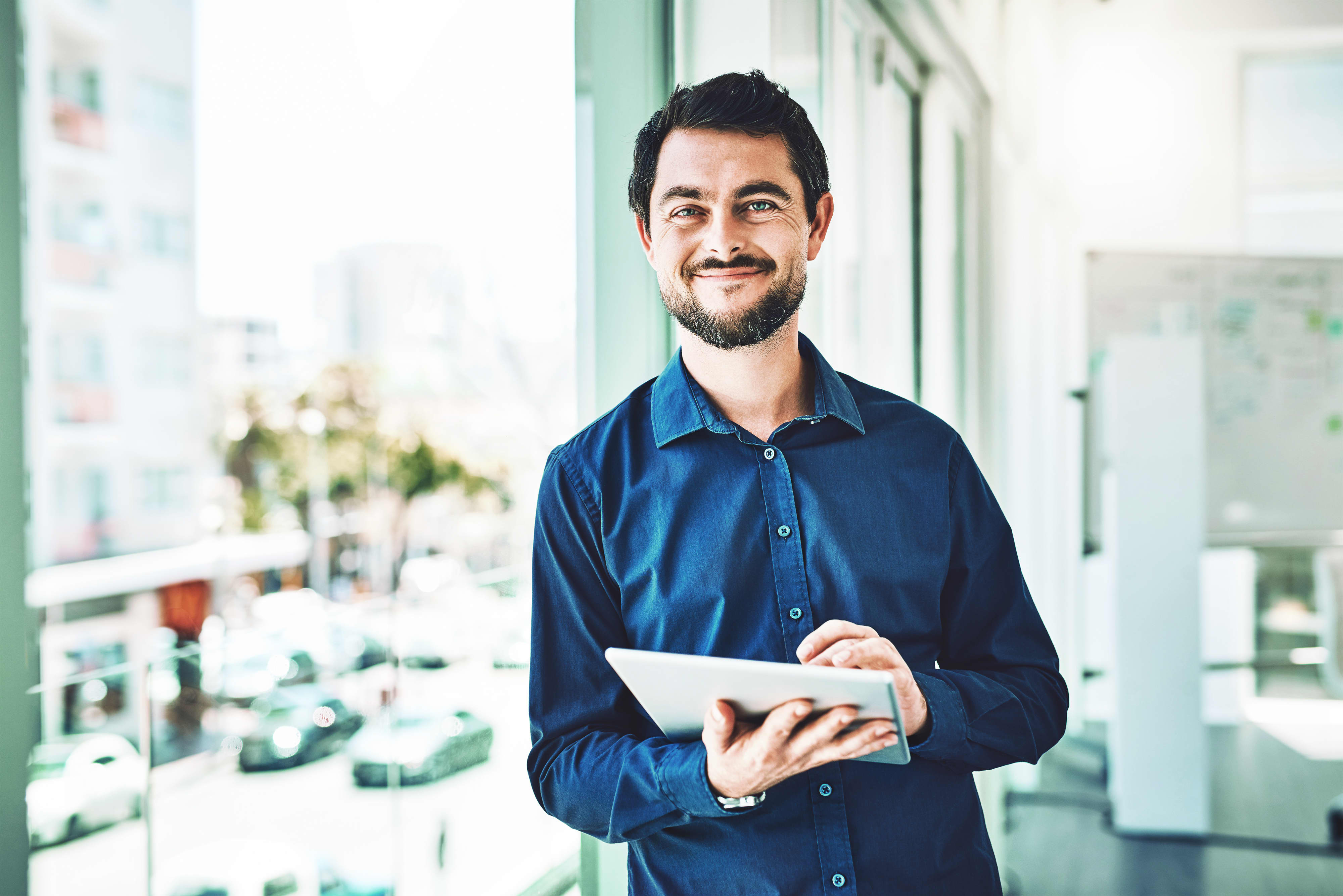 Titelbild für Infoseite “MBA - Digital Business”: Business Manager steht mit Tablet am Fenster