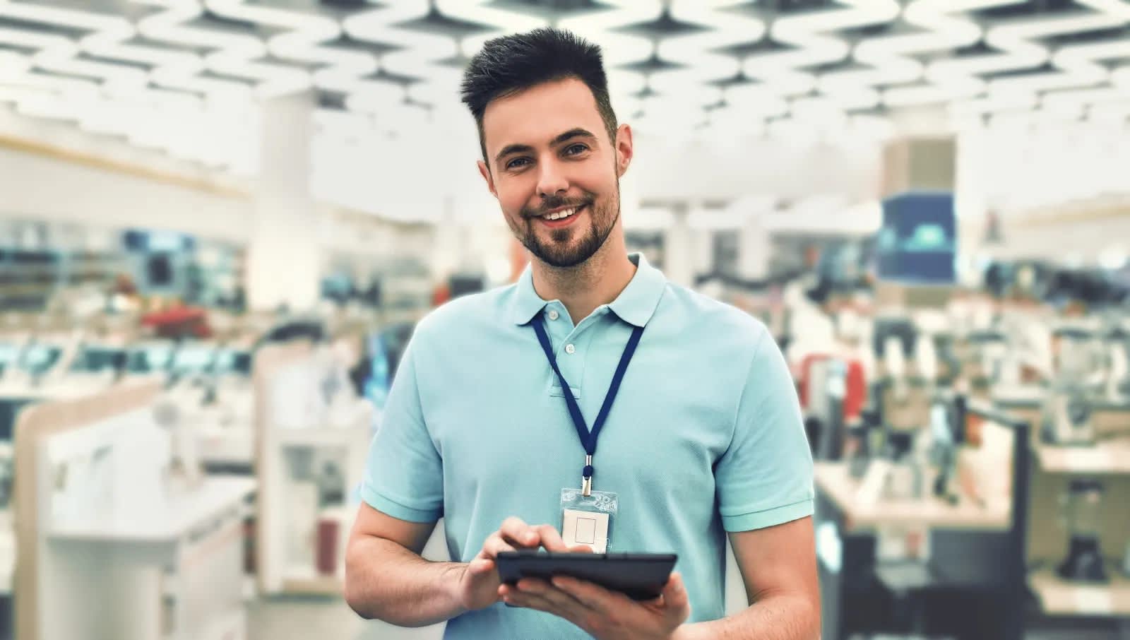 Titelbild für Infoseite “duales Studium BWL Handelsmanagement": Lächelnder dualer Student im Elektronikgeschäft mit Tablet in der Hand