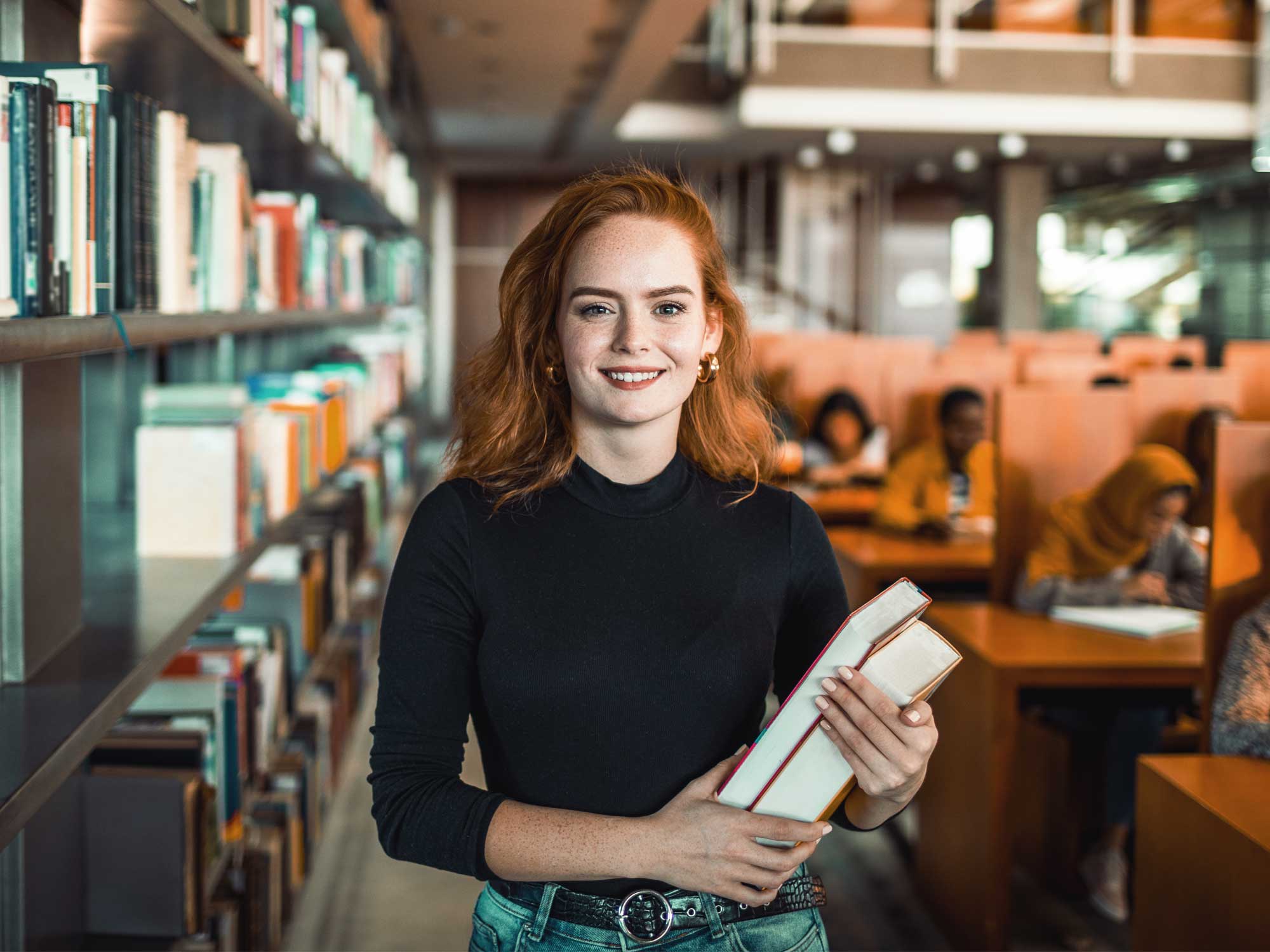 Titelbild für Infoseite "Lehrkonzepte und Methoden": Studentin mit Büchern in der Hand in der Bibliothek