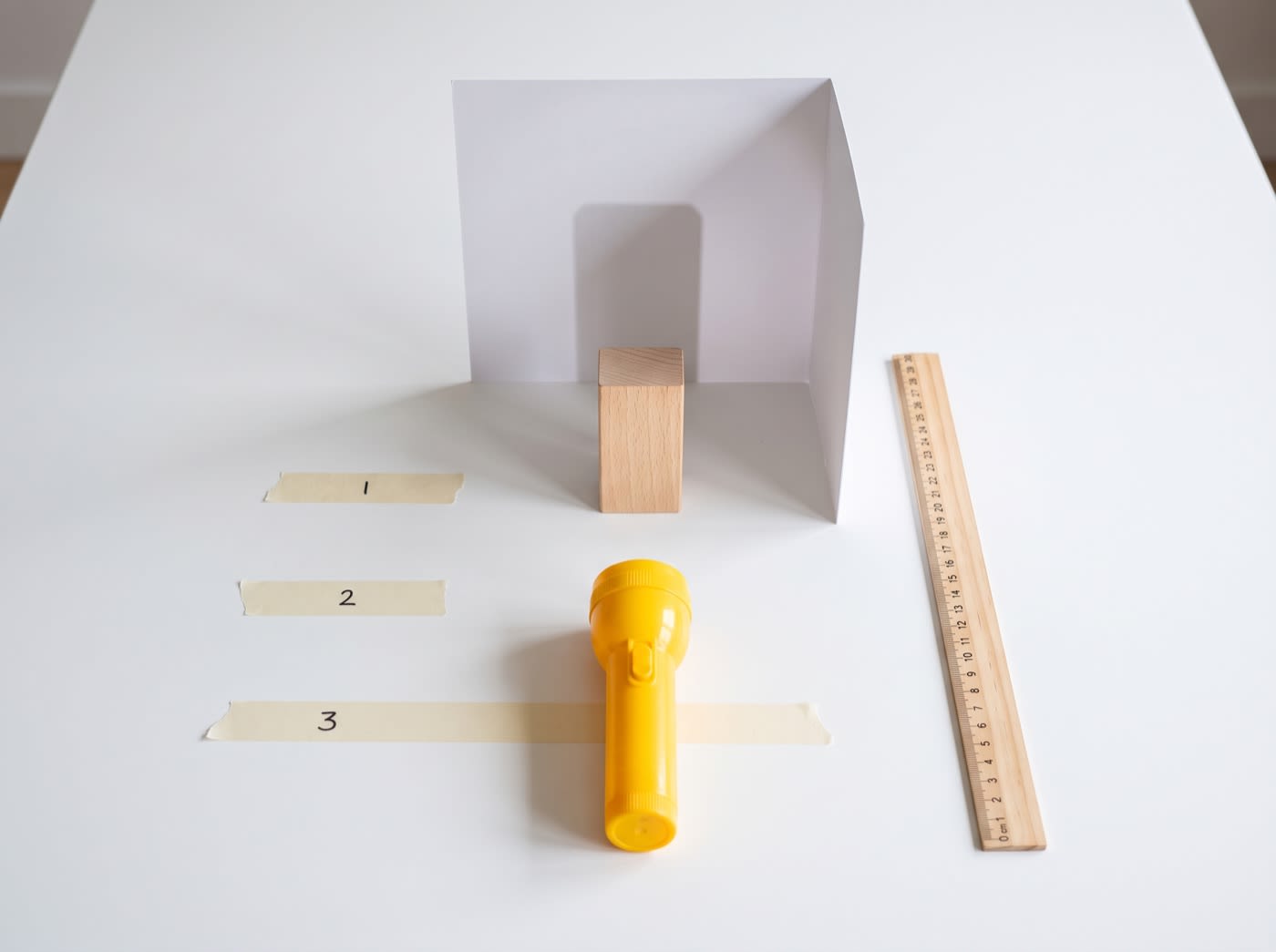 A flashlight on the first of three tape marks in front of a wooden block and a card screen