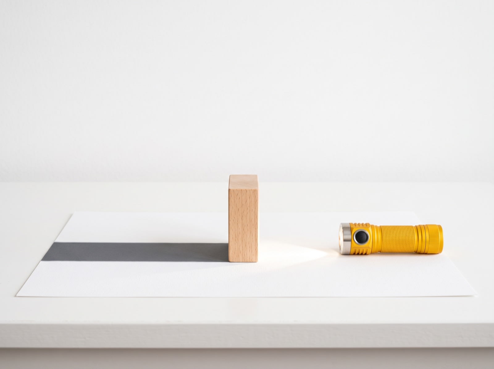 A yellow flashlight shining on a wooden block, which casts a shadow