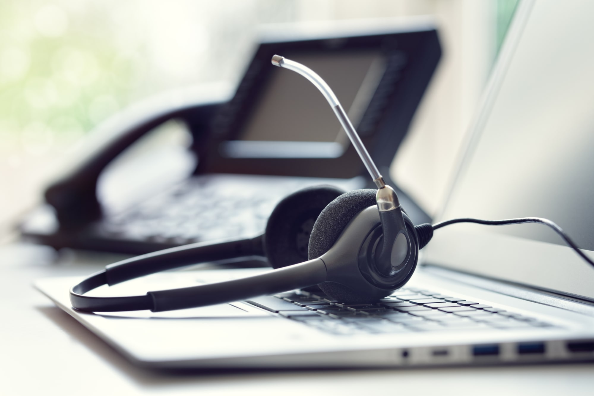 Nahaufnahme Laptop mit Headset und Systemtelefon im Hintergrund