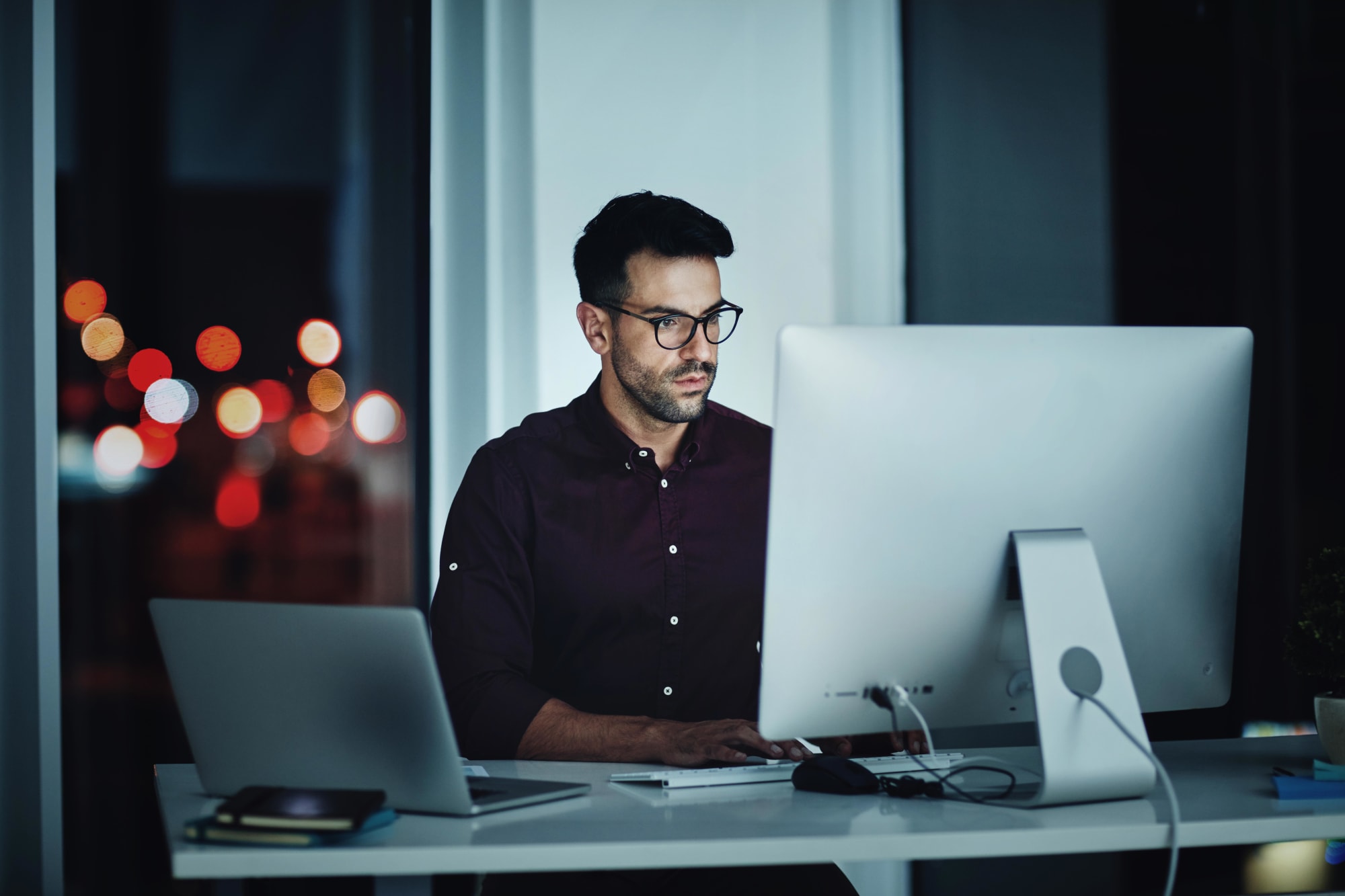 Mann arbeitet nachts am PC und Laptopim Büro