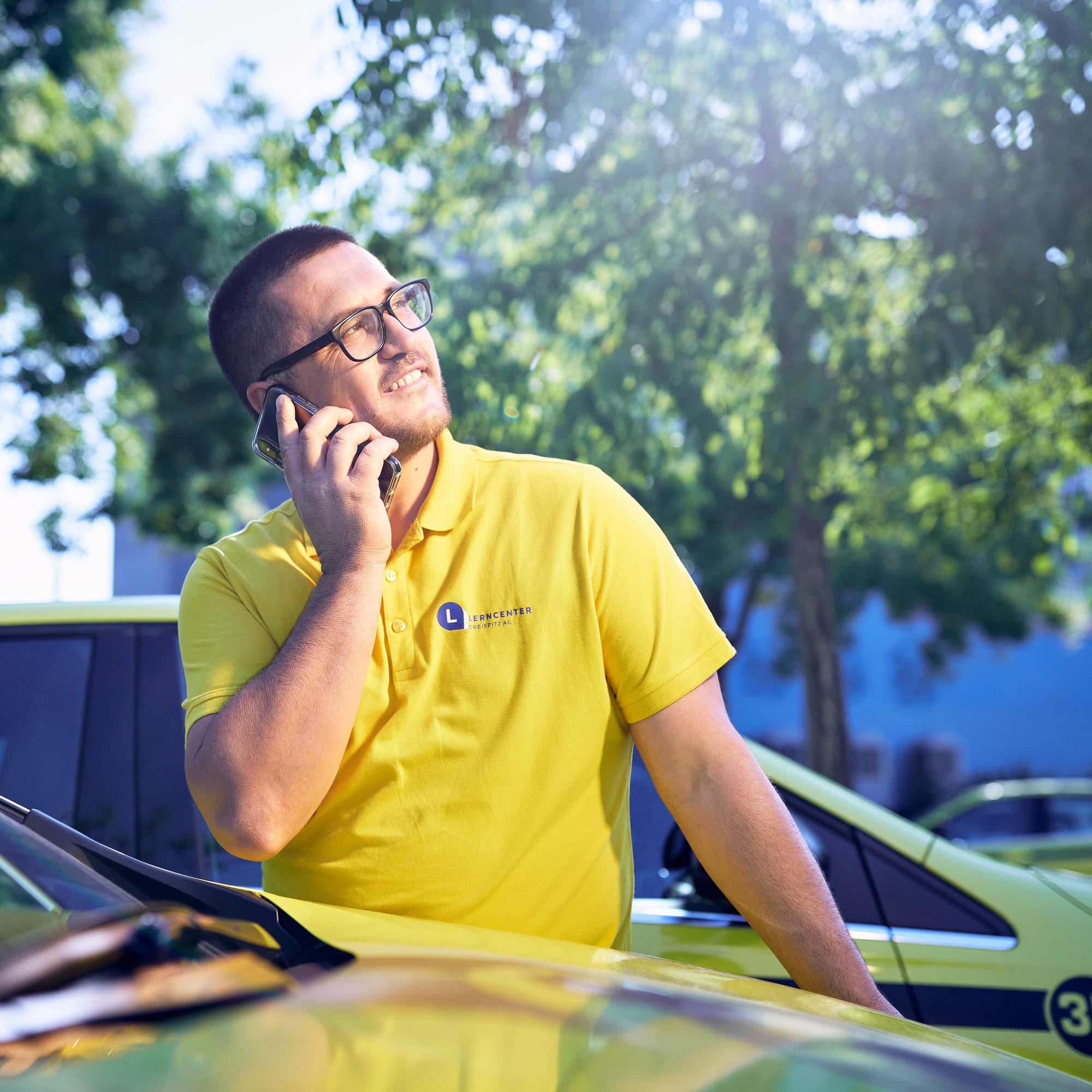 Fahrschullehrer fuehrt ein Telefonat an einem seiner Autos