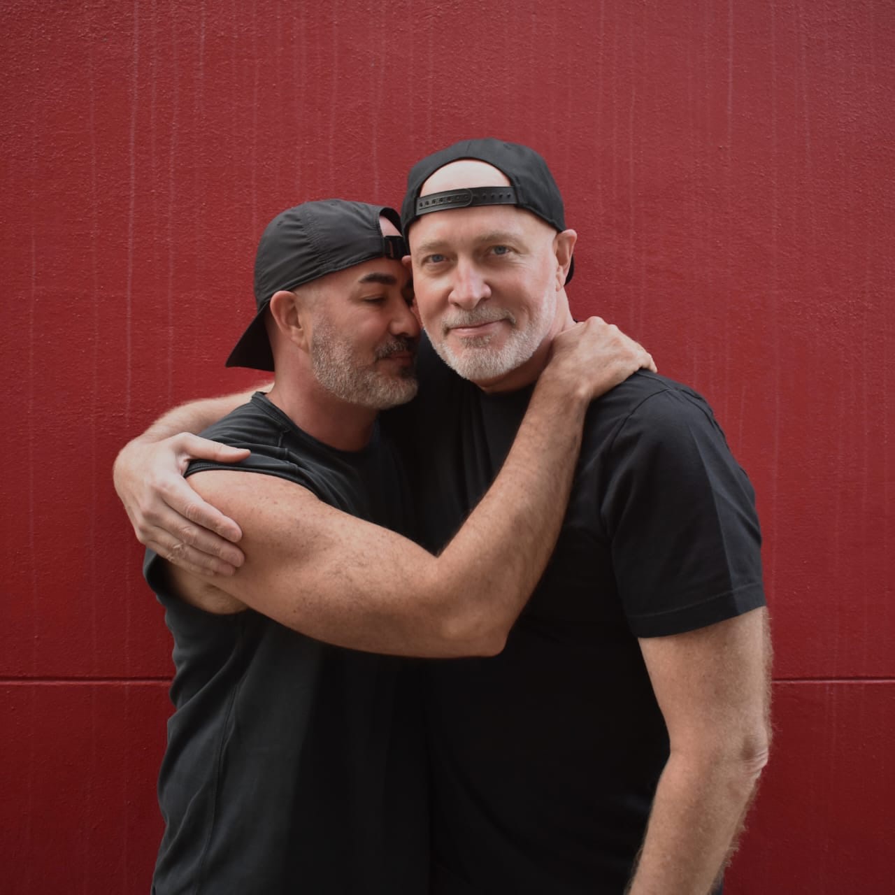 Adrian and Corey embracing against a deep red wall