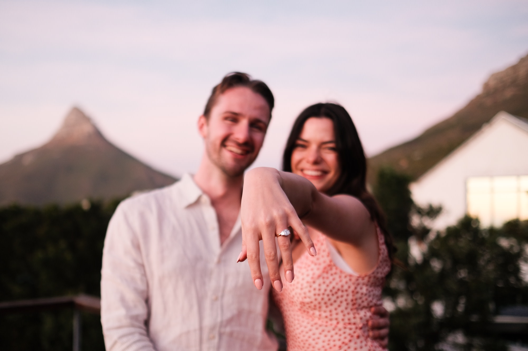 She shows off the engagement ring, both beaming, Lion's Head behind