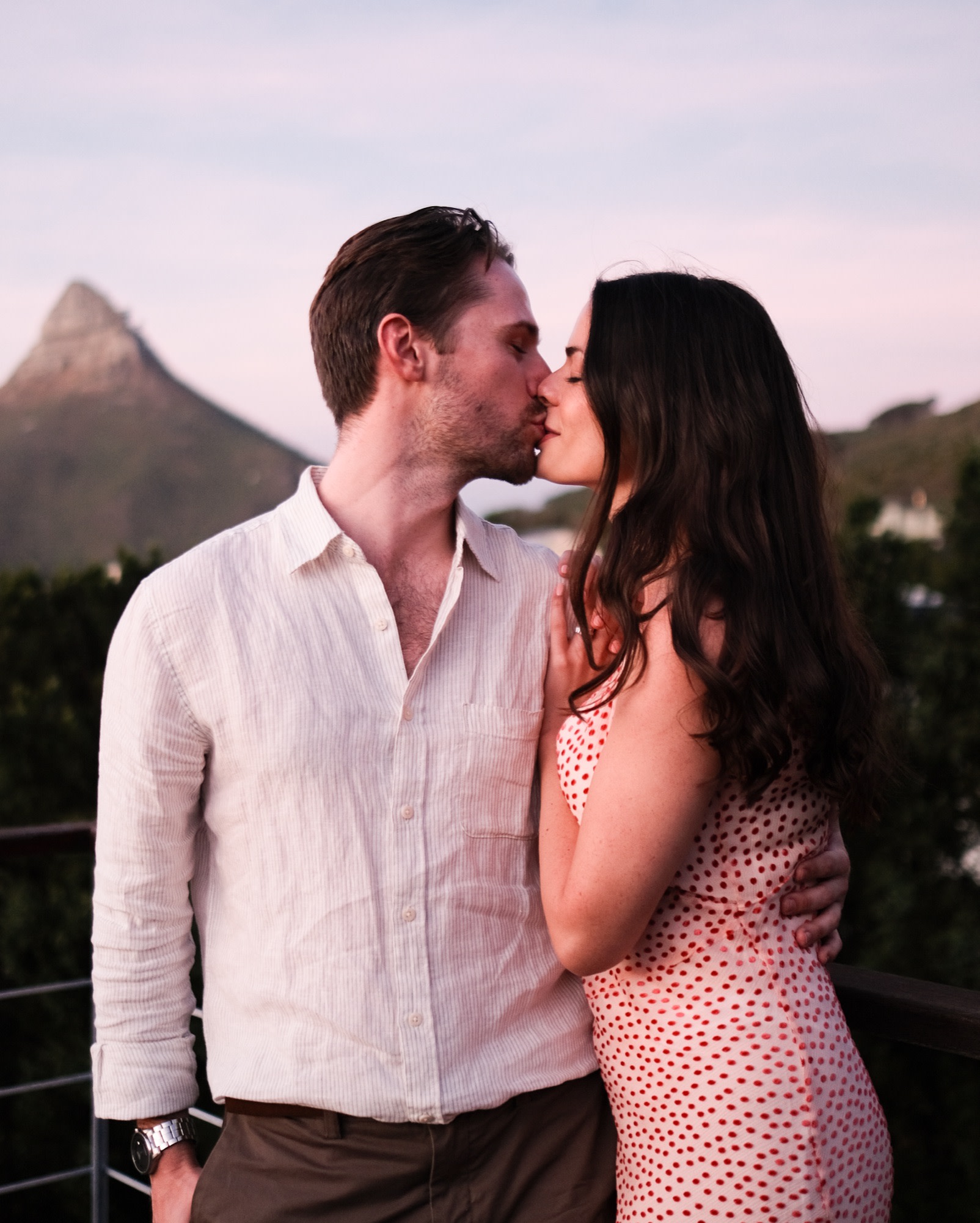 The couple kiss on a rooftop at sunset