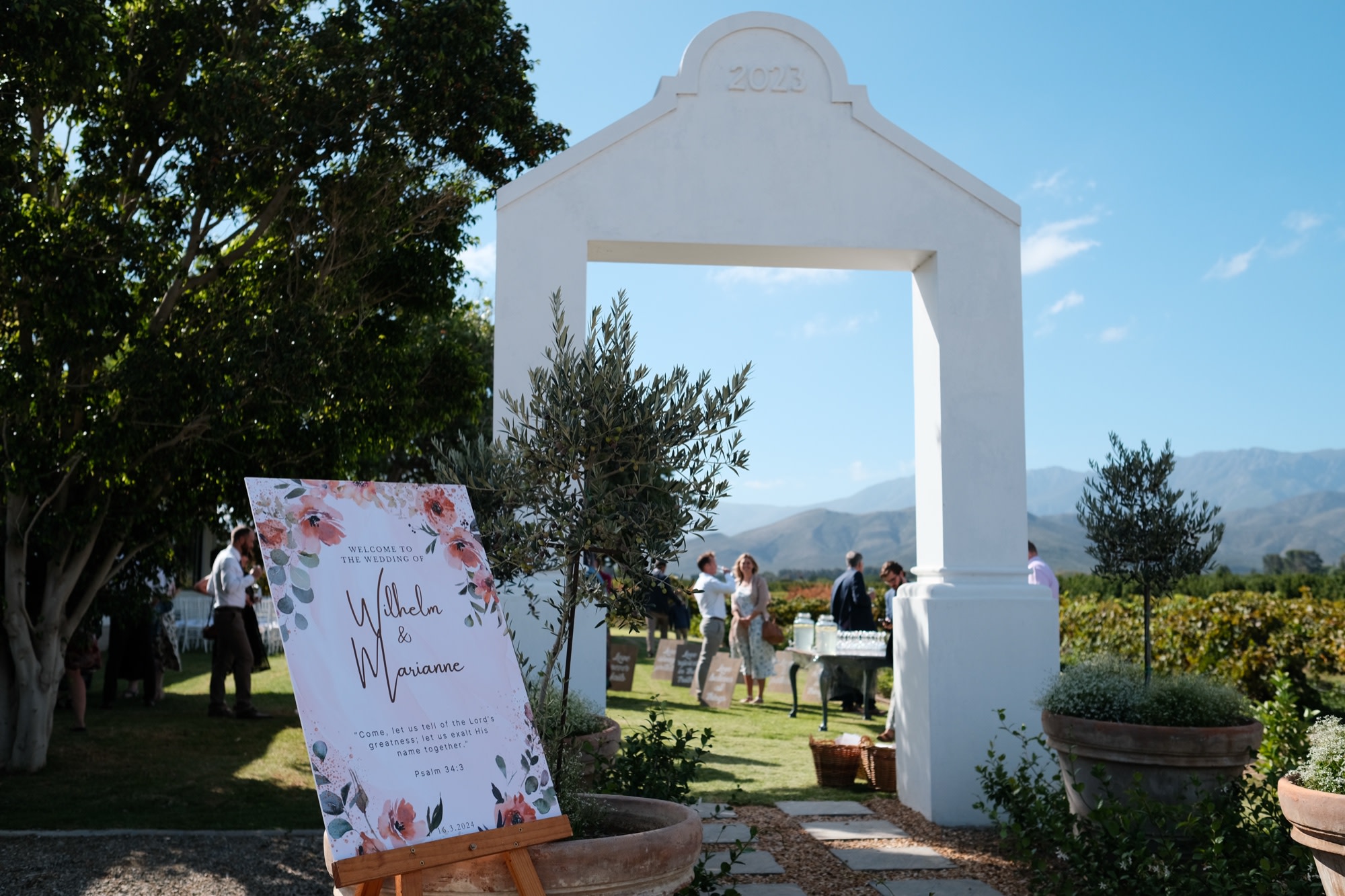 The venue welcome sign for Wilhelm & Marianne beneath a whitewashed arch, vineyards and mountains beyond