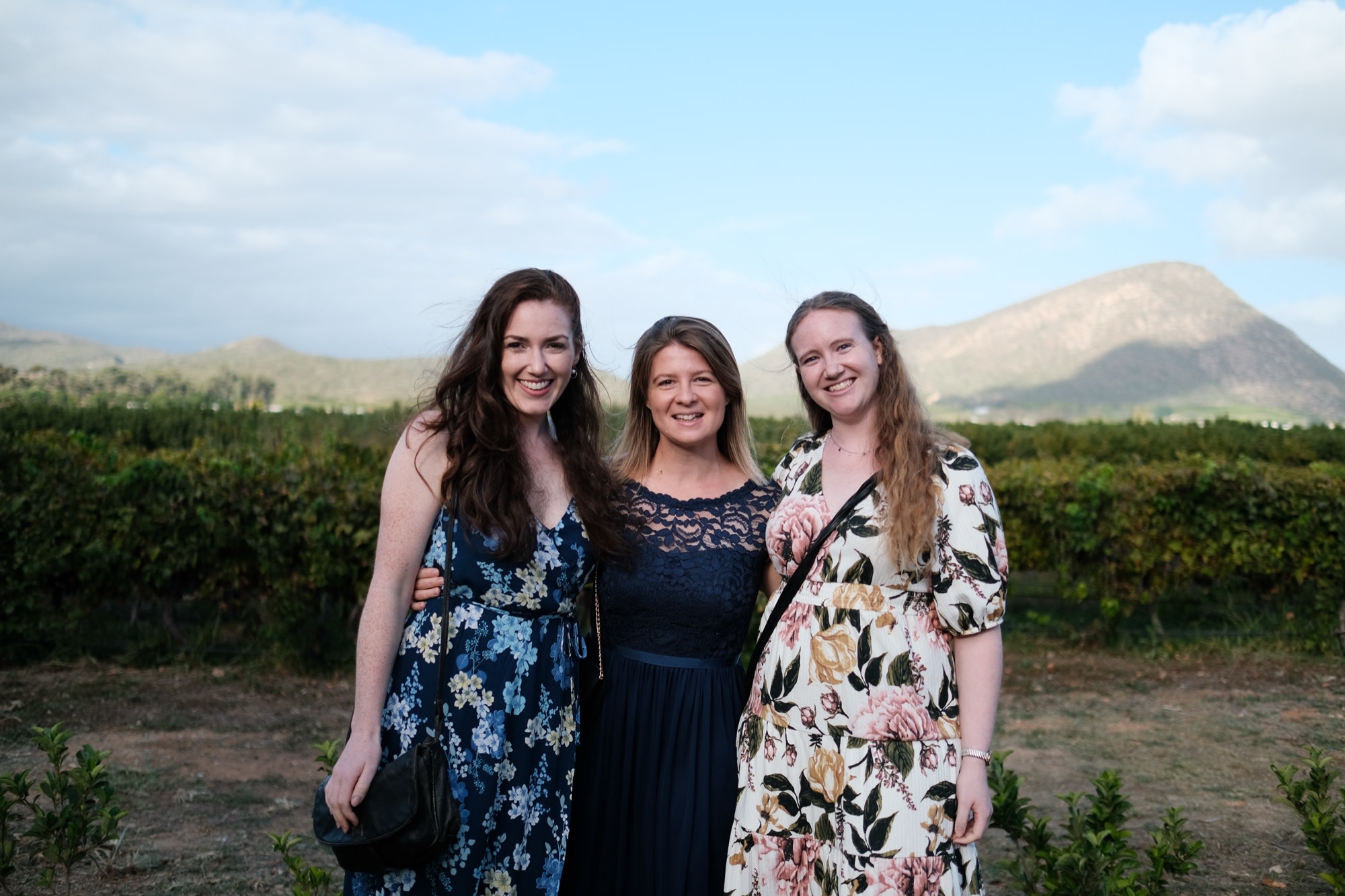 Three women guests together in front of the vines and mountains