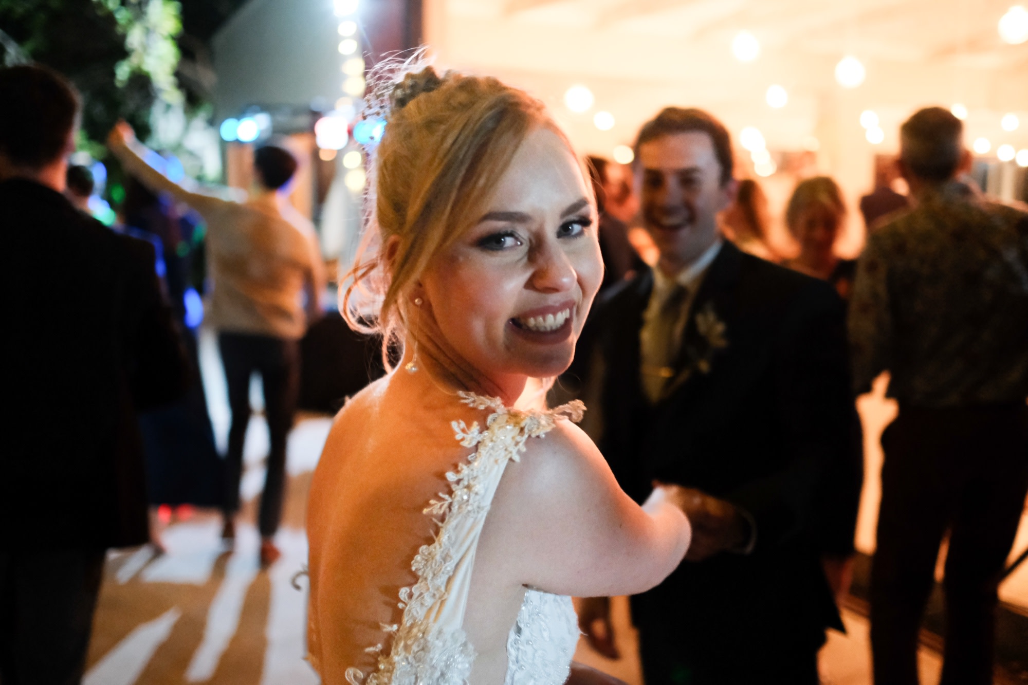 The bride glancing back on the fairy-lit dance floor at night
