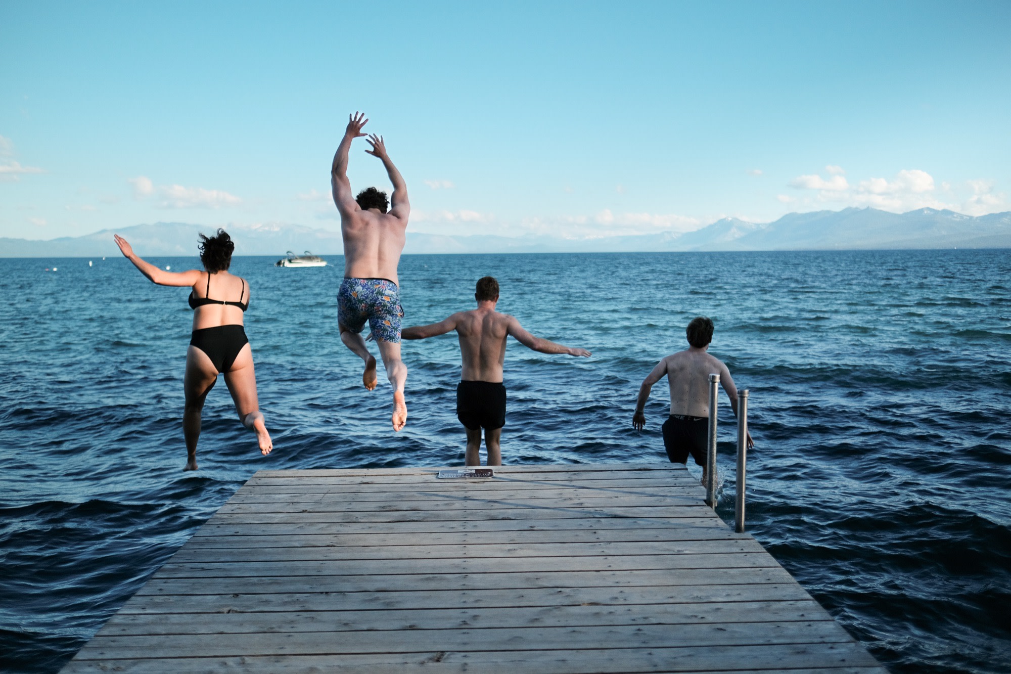Four friends leaping off a dock into an alpine lake