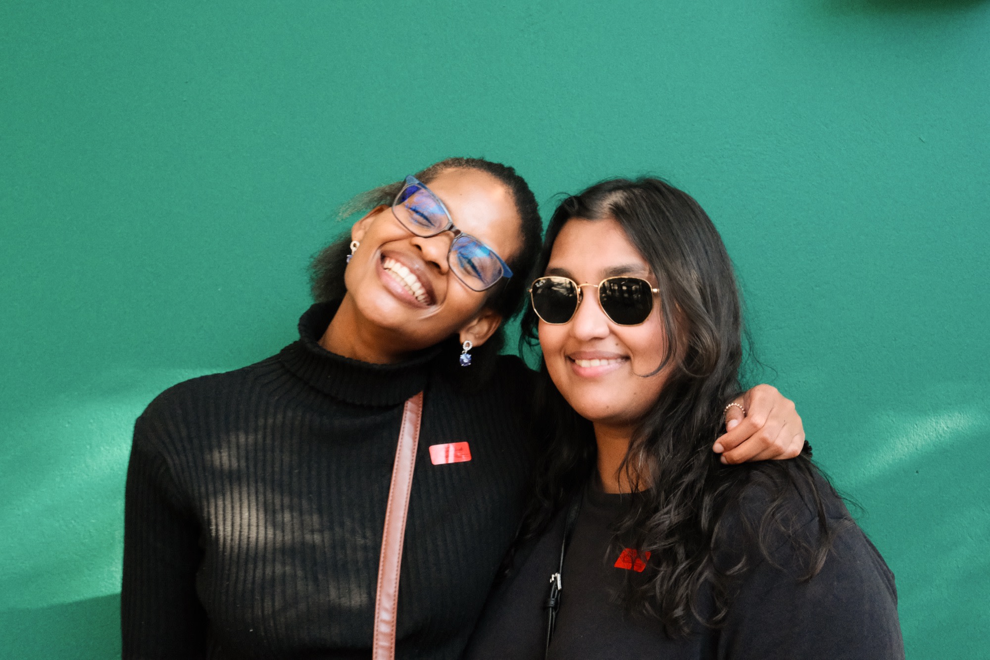 Two friends hugging against a bright green wall